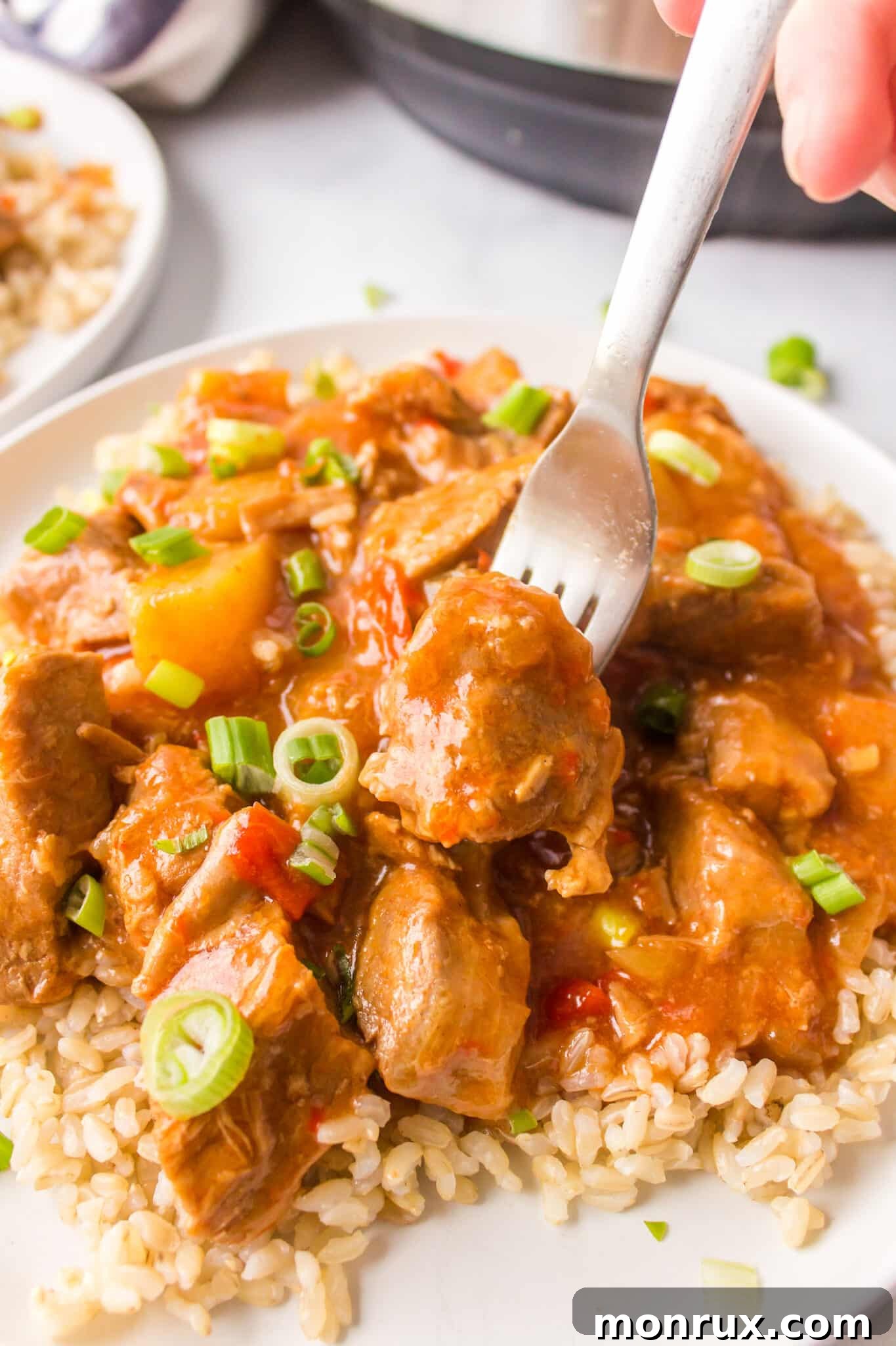 A fork with a bite of sweet and sour pork over a plate of brown rice.