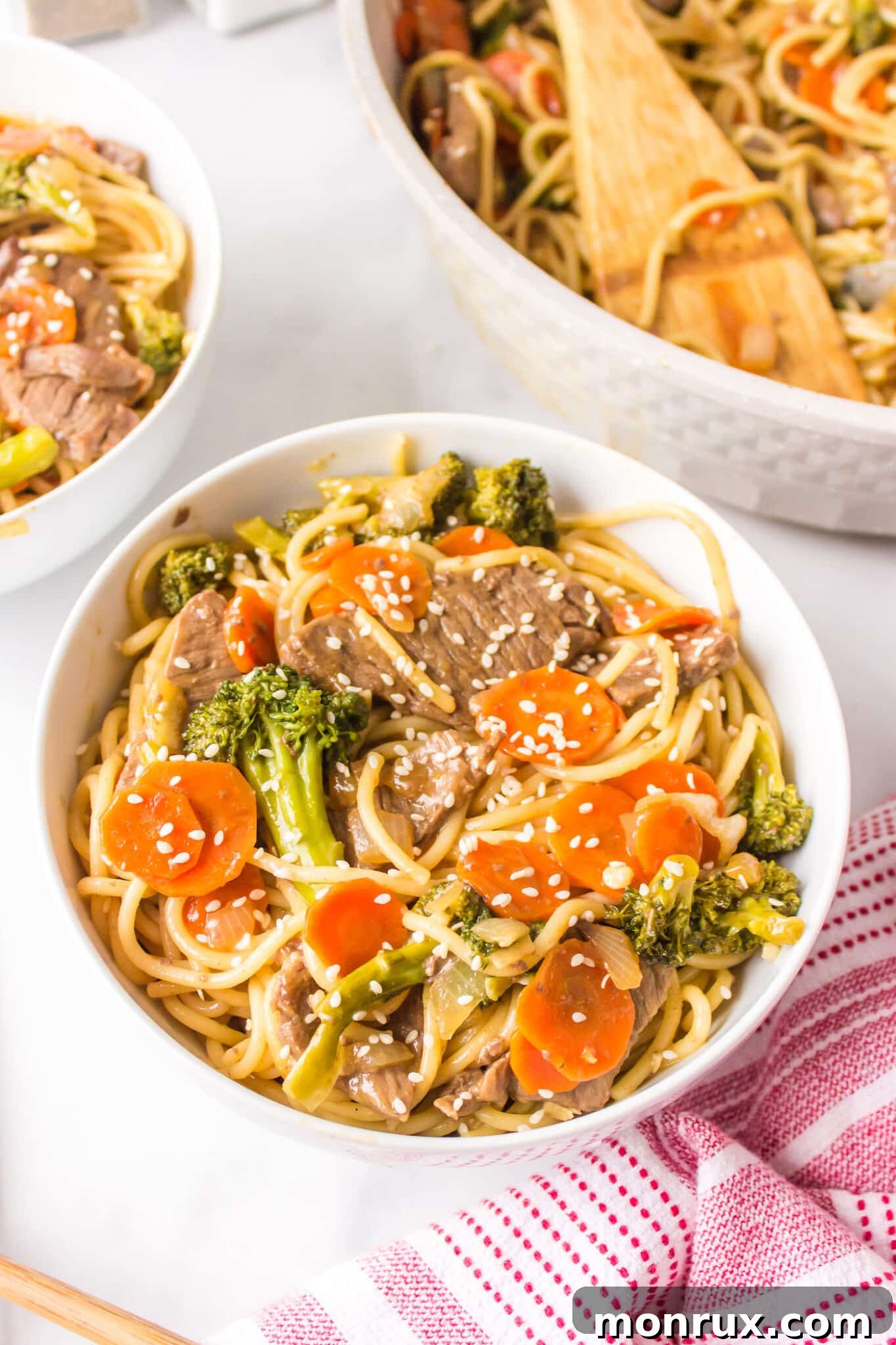 A beautifully presented white bowl of gluten-free teriyaki beef with tender noodles and crisp vegetables.