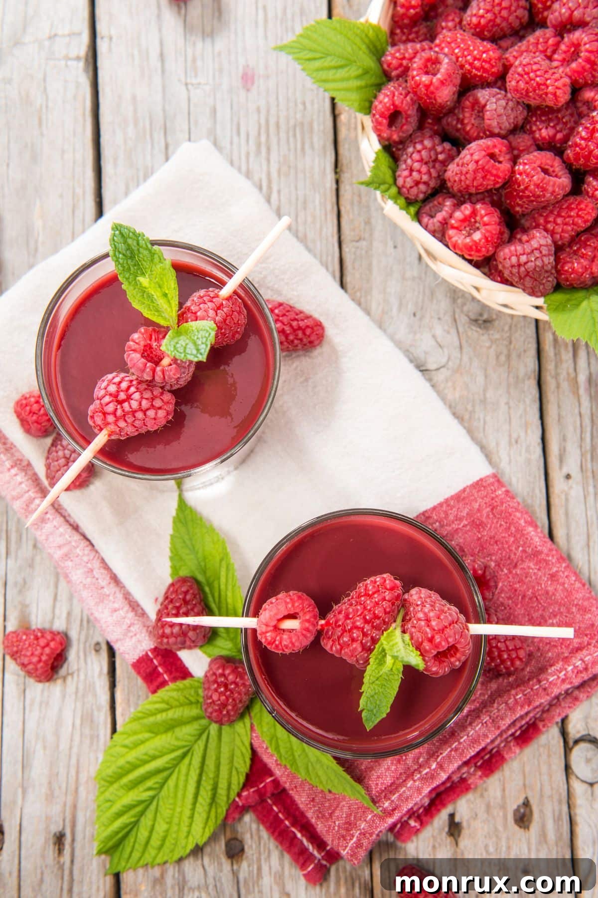 Top view of two elegant glasses of raspberry juice, garnished with mint, placed on a white towel.