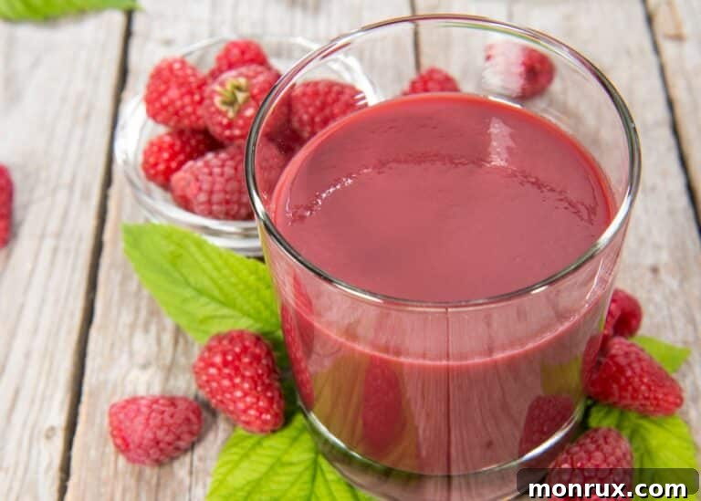 A glass of homemade raspberry juice on a wooden table, with fresh raspberries in the background.