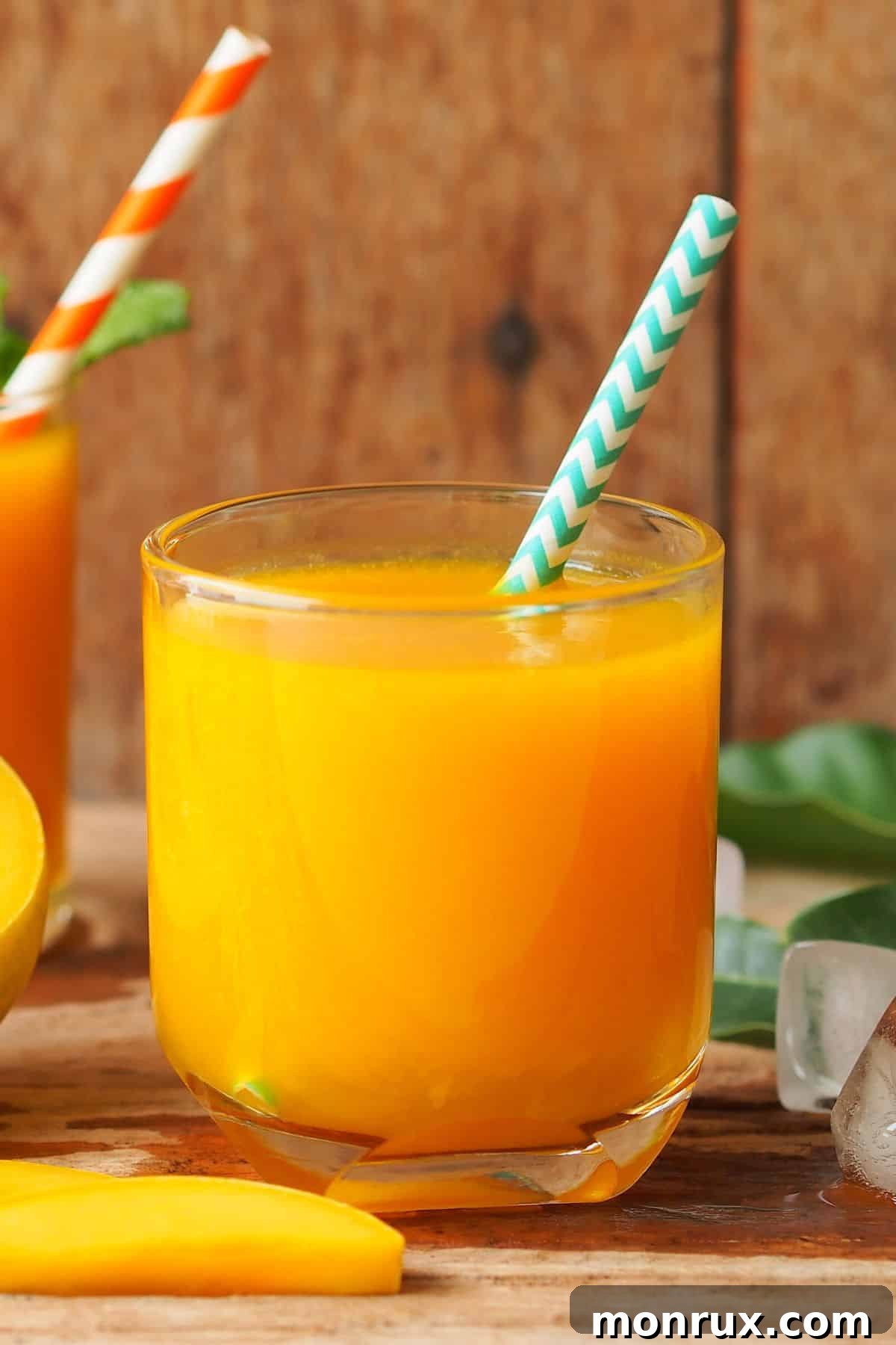A short glass of mango carrot juice with a striped straw.
