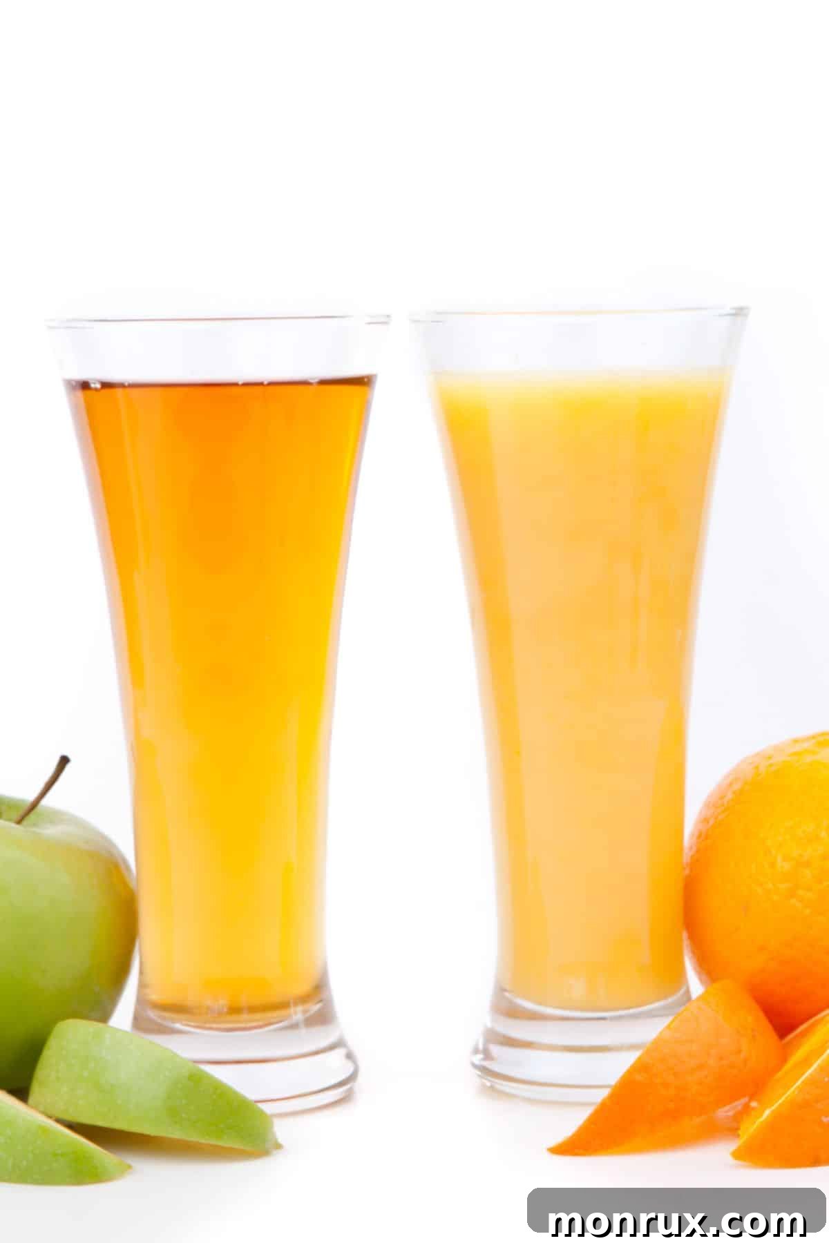 Two tall glasses, one of orange juice and one of apple juice, sitting on a wooden table.