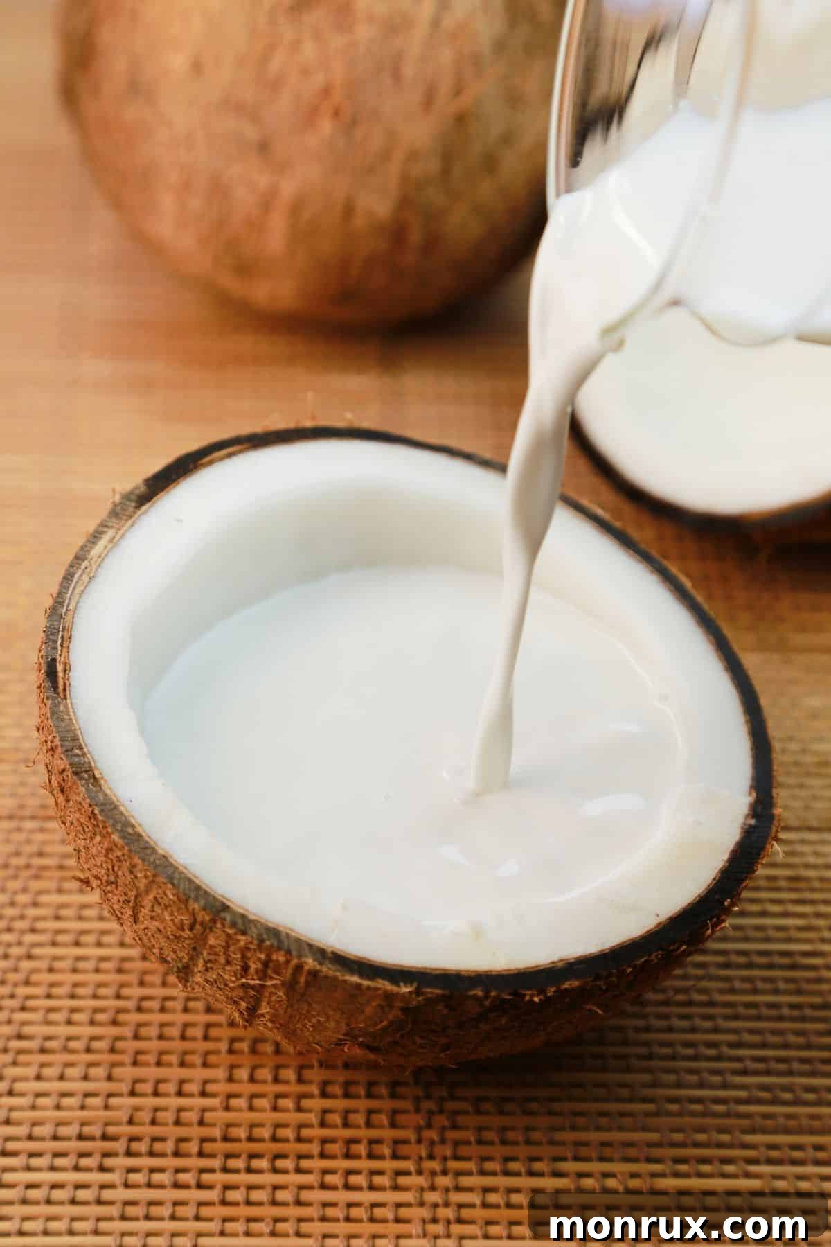 Fresh coconut milk being poured into a half coconut shell, illustrating its creamy texture.