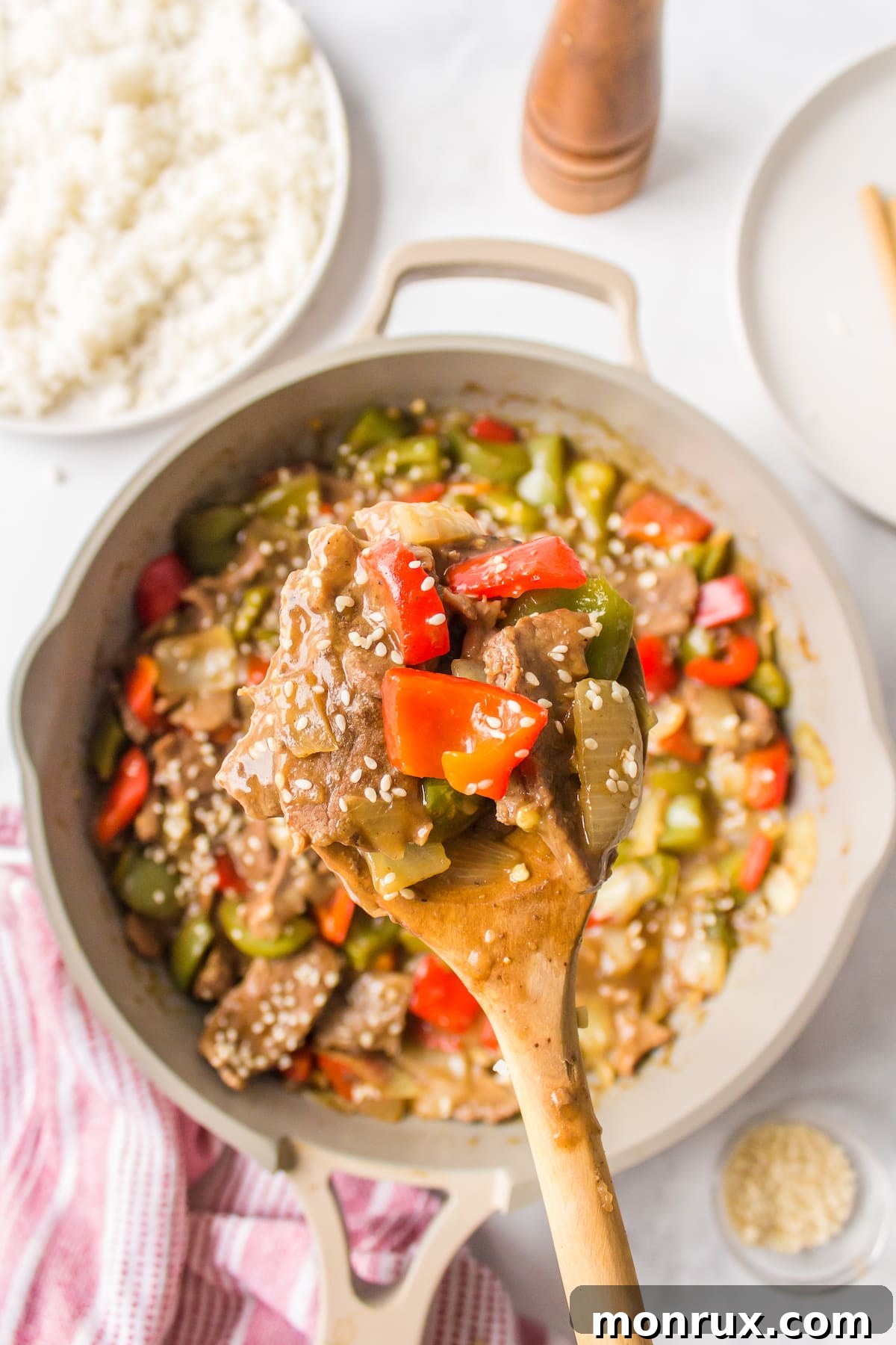a serving spoon dishing out P.F. Chang's style pepper steak onto a plate, showcasing the glossy sauce and tender ingredients.
