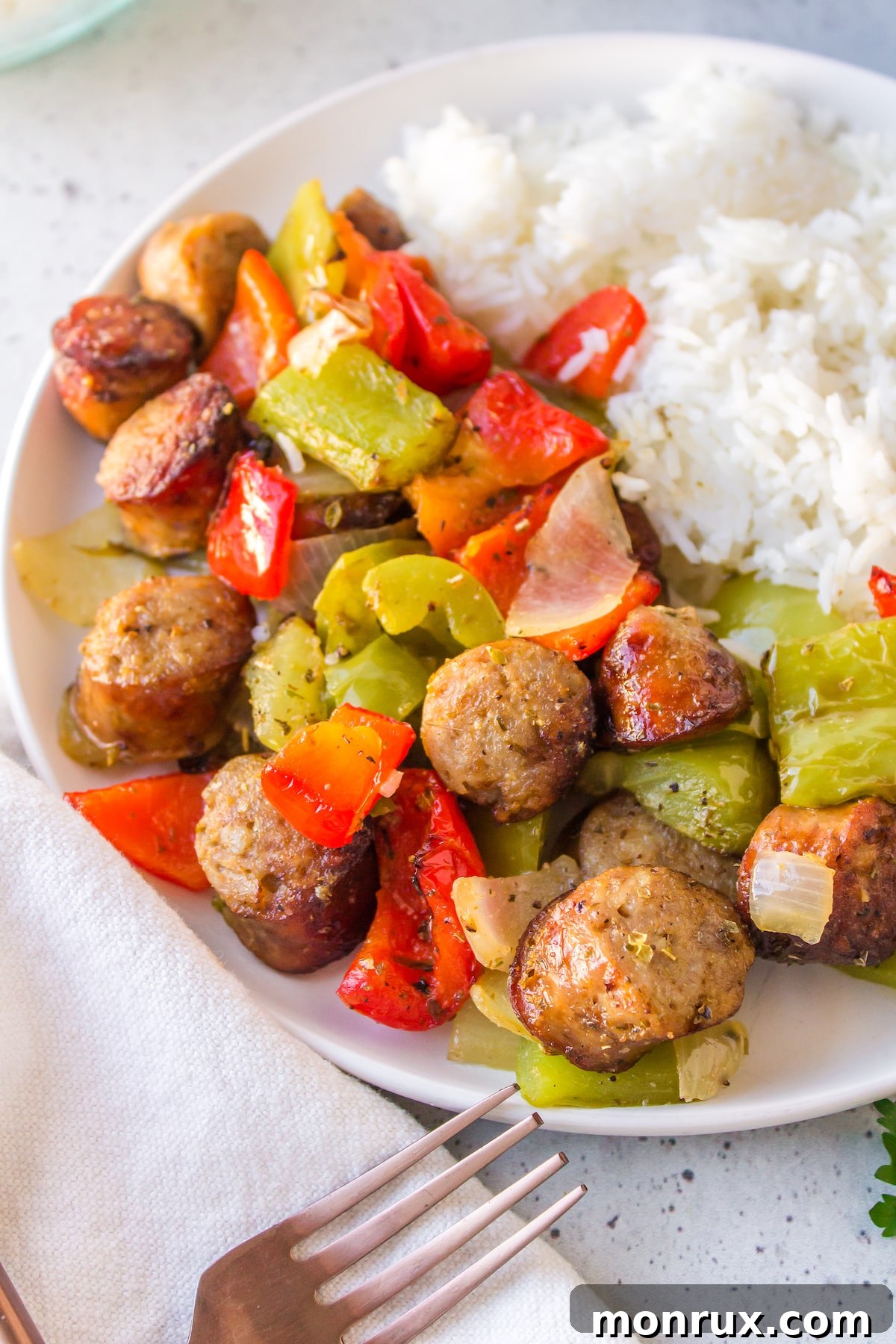 A serving of perfectly cooked air fryer sausage and peppers on a white plate, accompanied by fluffy white rice, ready to be enjoyed as a wholesome and quick dinner.