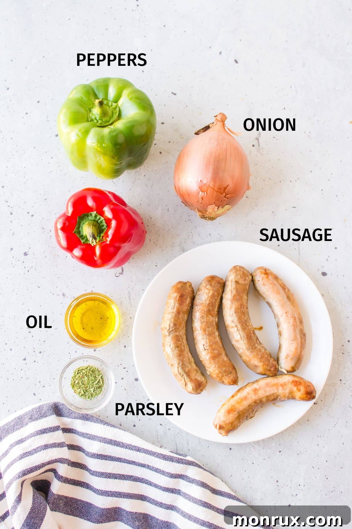 A beautiful flat lay of fresh ingredients laid out on a clean white countertop, including Italian sausages, vibrant red and green bell peppers, a white onion, a bottle of olive oil, and a small dish of dried parsley, all ready for cooking.