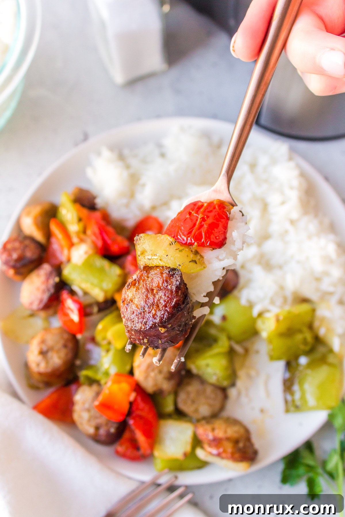 A close-up shot of a person using a fork to pick up a piece of perfectly air-fried sausage and a vibrant bell pepper, showcasing the appetizing texture and golden-brown finish of the meal.