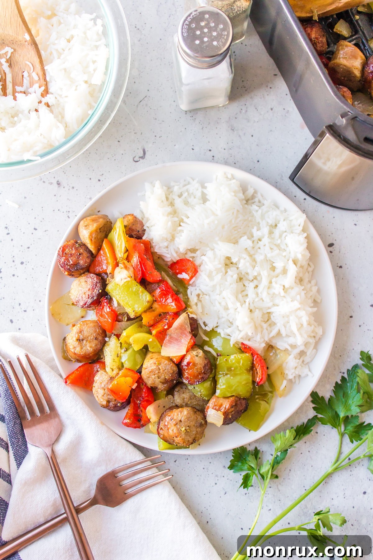An inviting overhead photograph of air fryer sausage and peppers artfully arranged on a pristine white plate, complemented by a serving of fluffy rice, creating a colorful and balanced meal.