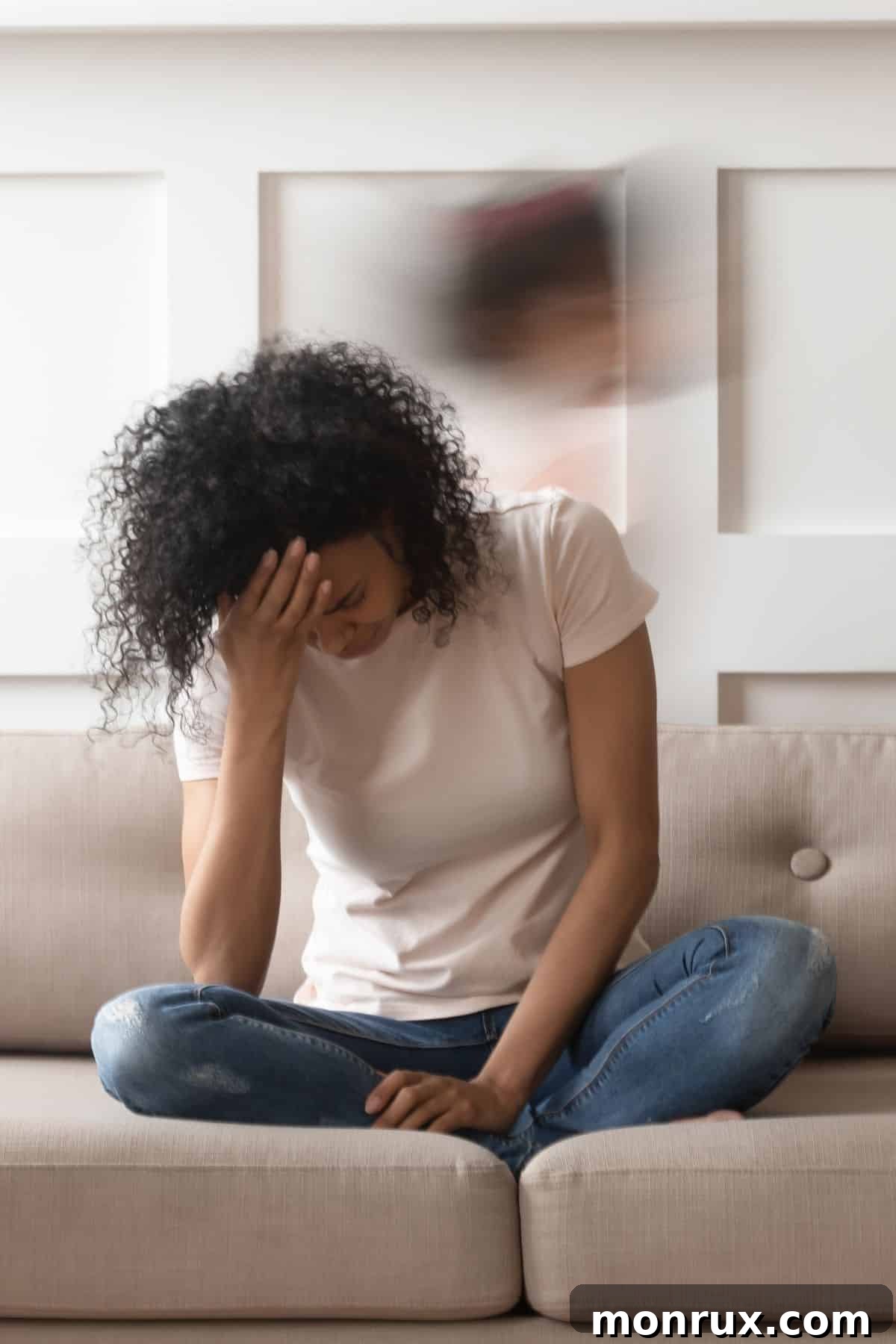 A tired woman on a couch holds her head in her hands, depicting fatigue.