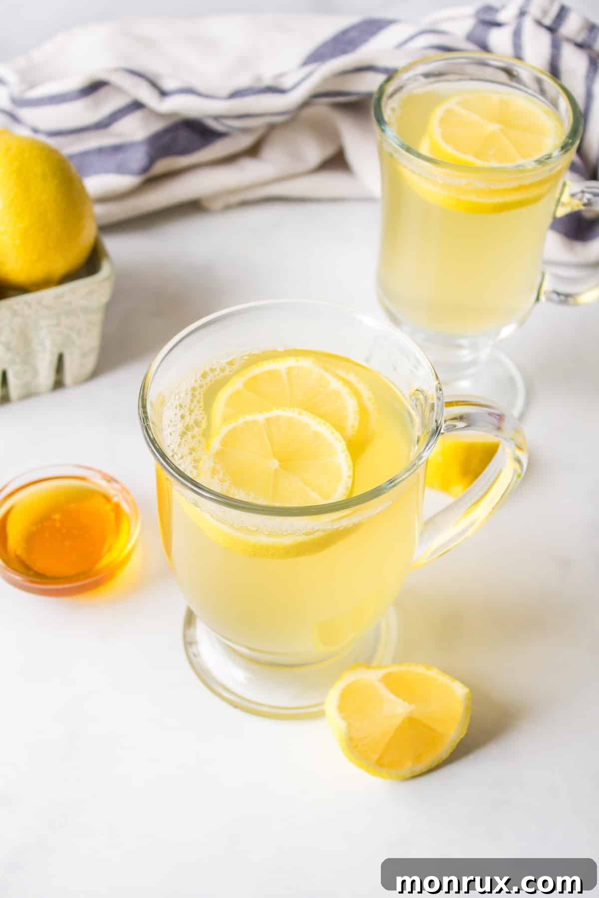 Clear mug with honey lemon tea topped with sliced lemon.