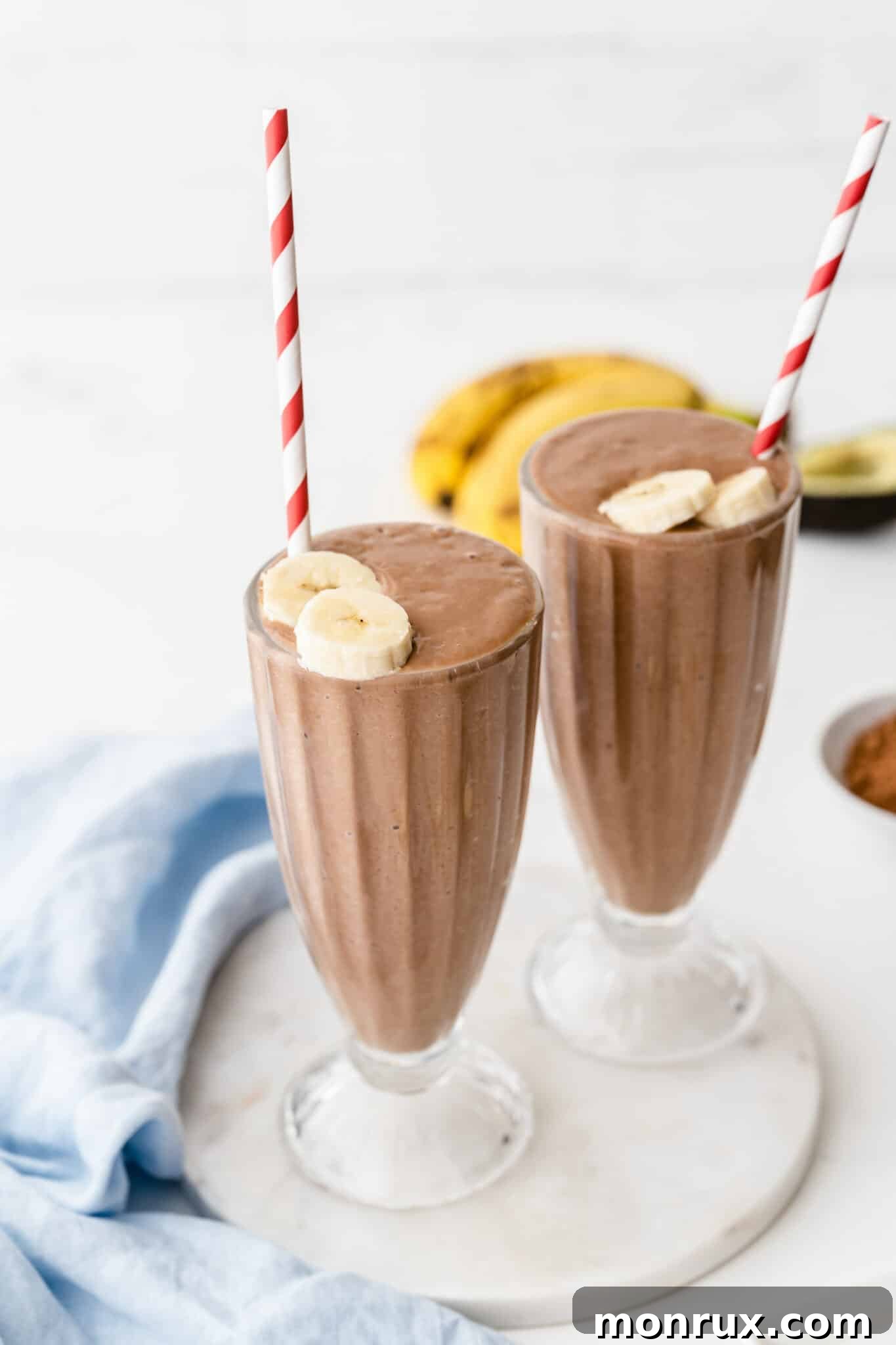 two glasses of avocado chocolate smoothie with straws.