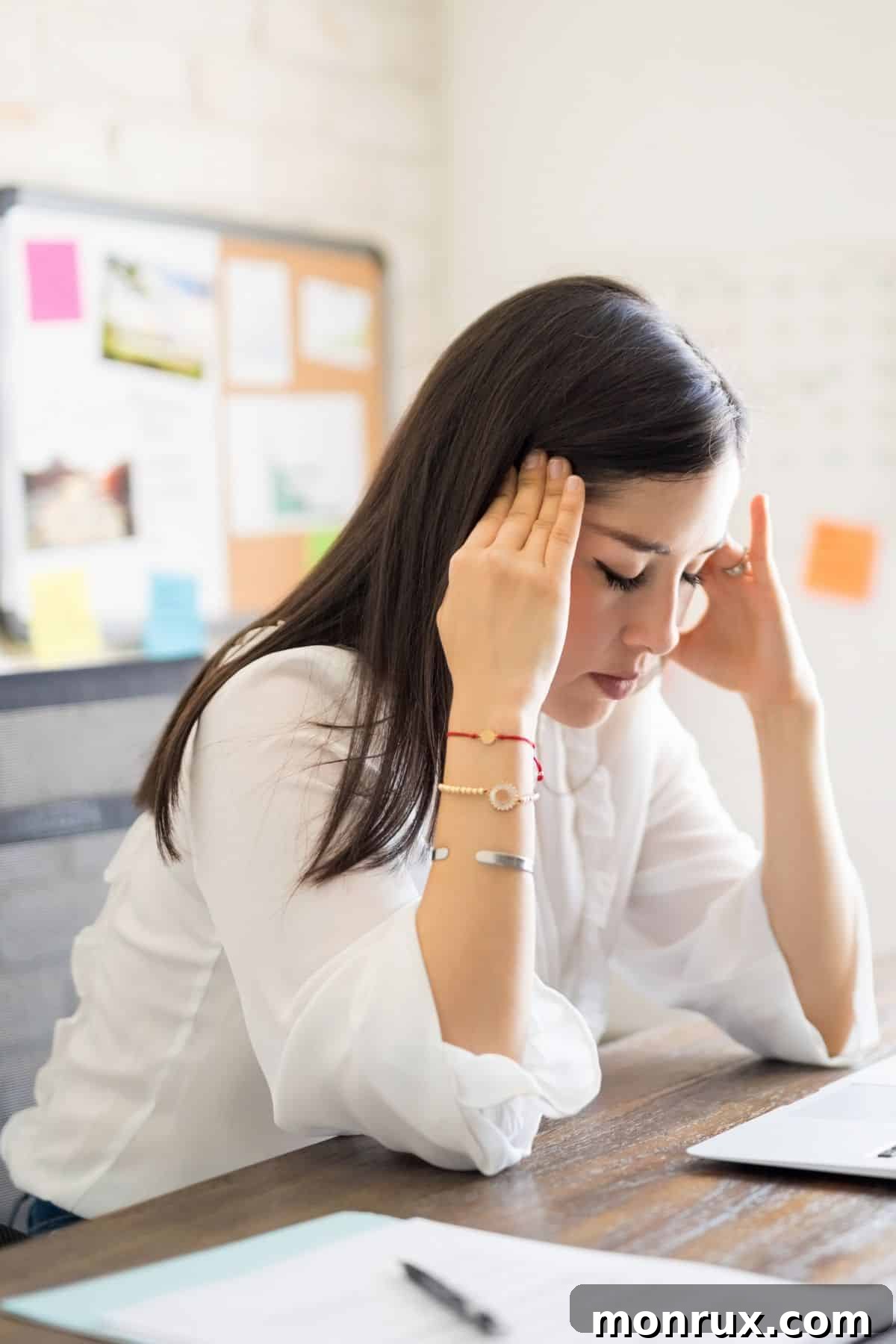 A woman sitting at her desk holding her head, experiencing a headache.