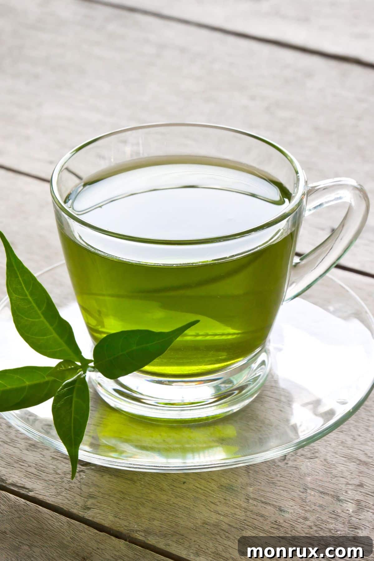 A clear mug of green tea on a wooden table, steam rising.