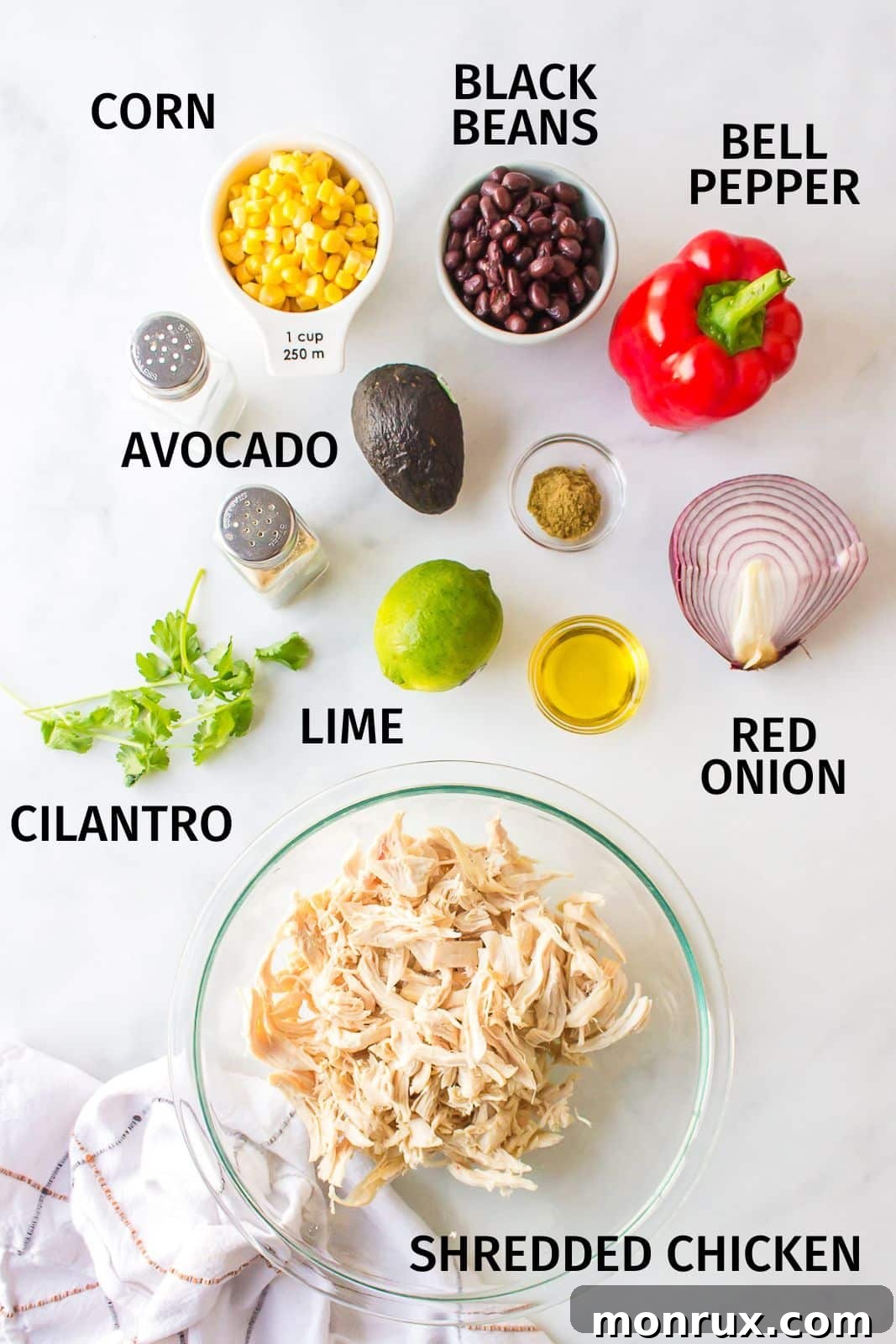 Fresh ingredients laid out on a kitchen counter, including shredded chicken, black beans, corn, bell pepper, and avocado, ready for a Mexican Chicken Salad.