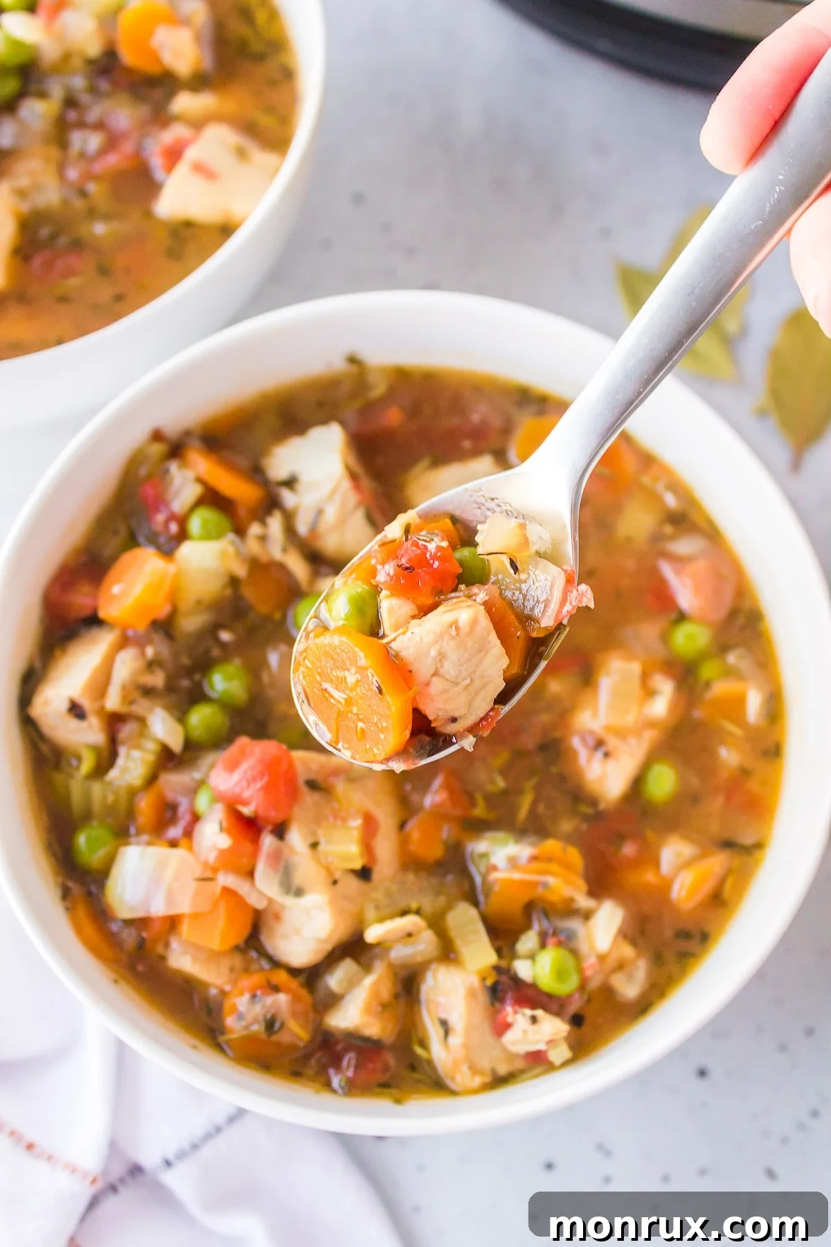 A close-up shot of a spoon scooping a portion of rich Instant Pot Chicken Stew, highlighting the tender chicken and colorful vegetables.