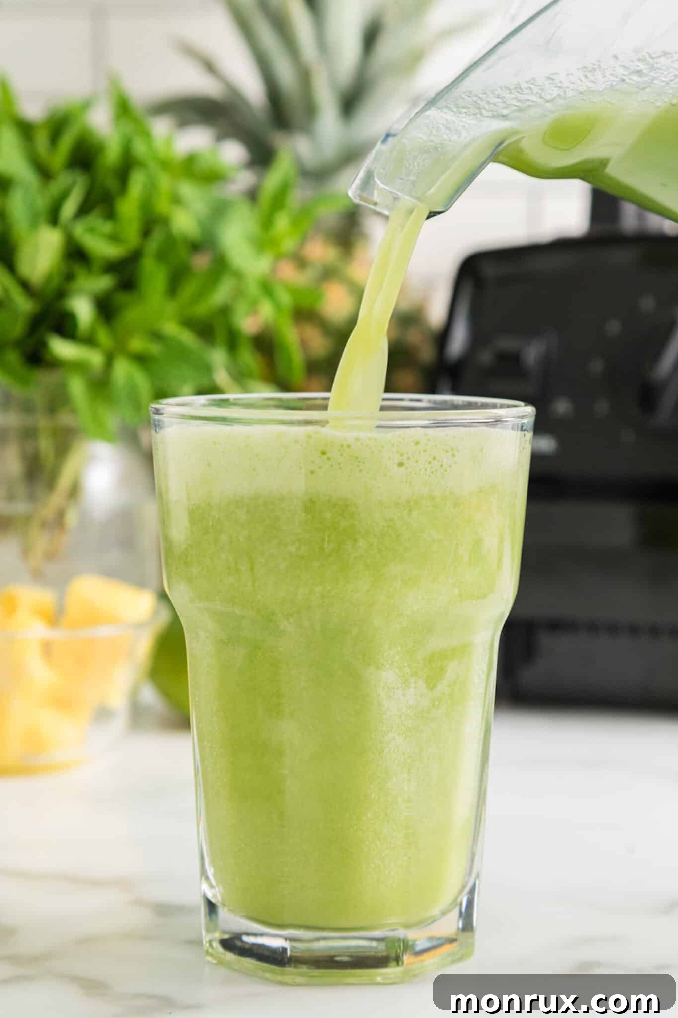 A vibrant cucumber pineapple smoothie being poured into a tall glass, garnished with a lime slice.