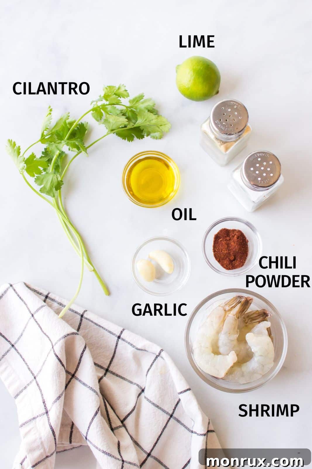 A rustic countertop displays the fresh ingredients for cilantro lime shrimp, including vibrant green limes, a bunch of fresh cilantro, and whole garlic cloves.