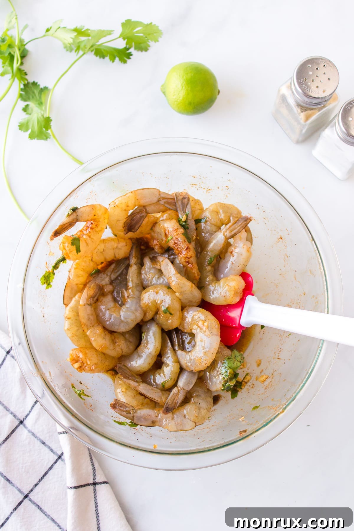 Raw shrimp marinating in a clear mixing bowl with olive oil, lime juice, garlic, cilantro, and spices.