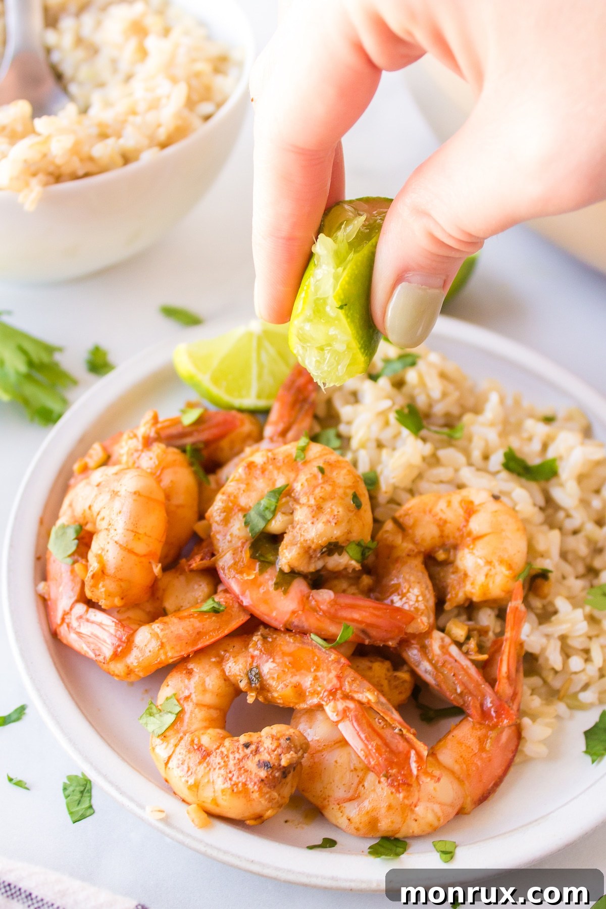 A hand squeezing a fresh lime wedge over a plate of perfectly cooked cilantro lime shrimp, adding a final touch of zest.