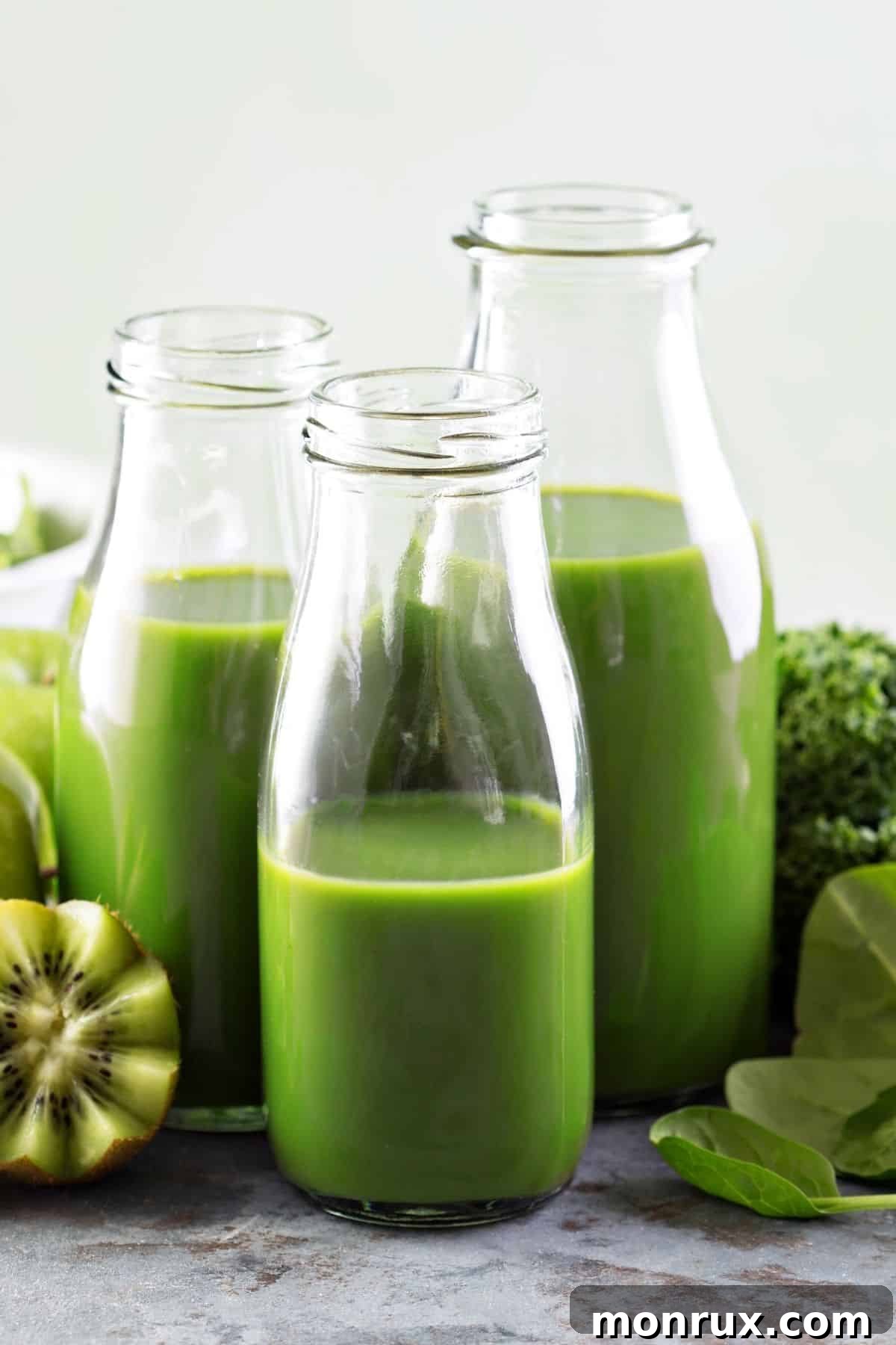Three vibrant green juices in glass jars on a rustic wooden table, garnished with fresh herbs, symbolizing natural relief from bloating.