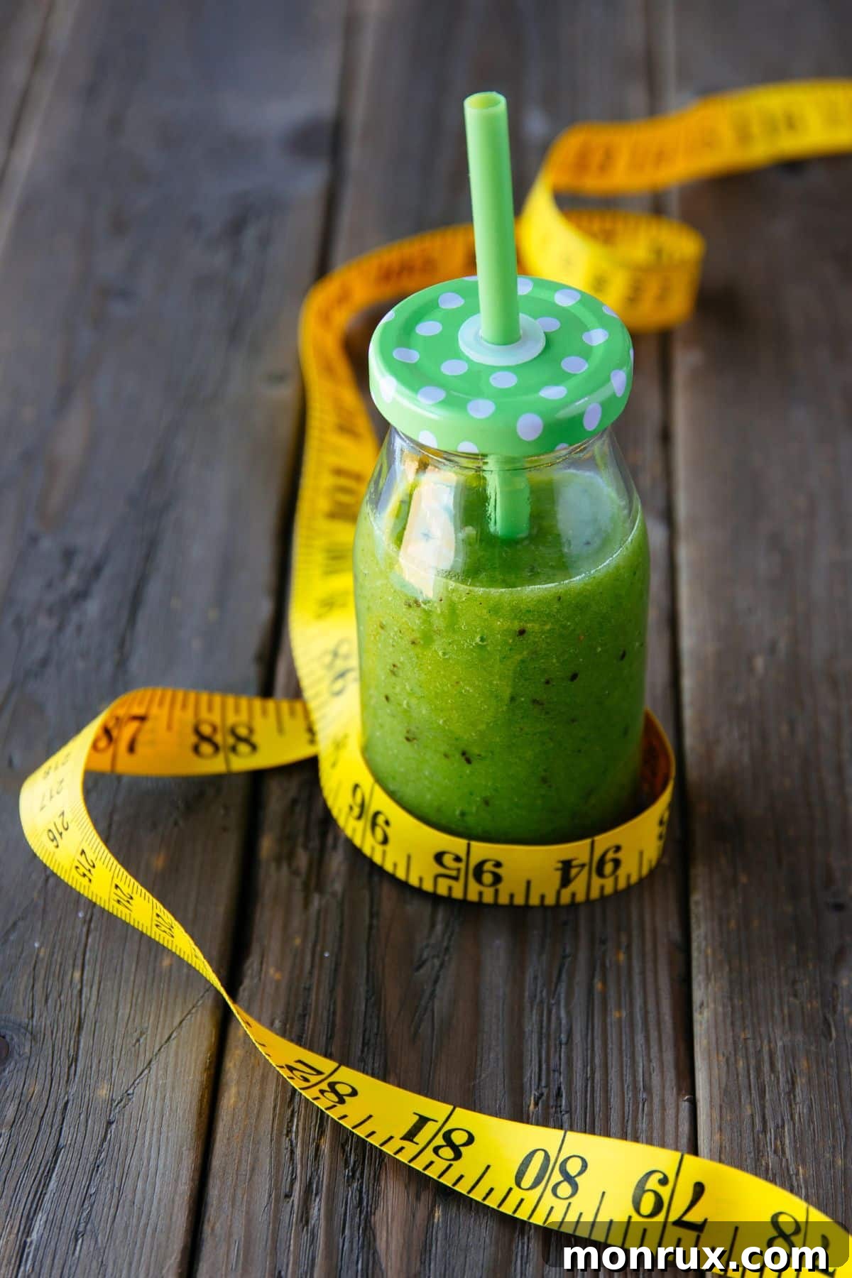 A vibrant green smoothie in a glass jar, accompanied by a measuring tape and fresh spinach leaves, symbolizing healthy weight loss.