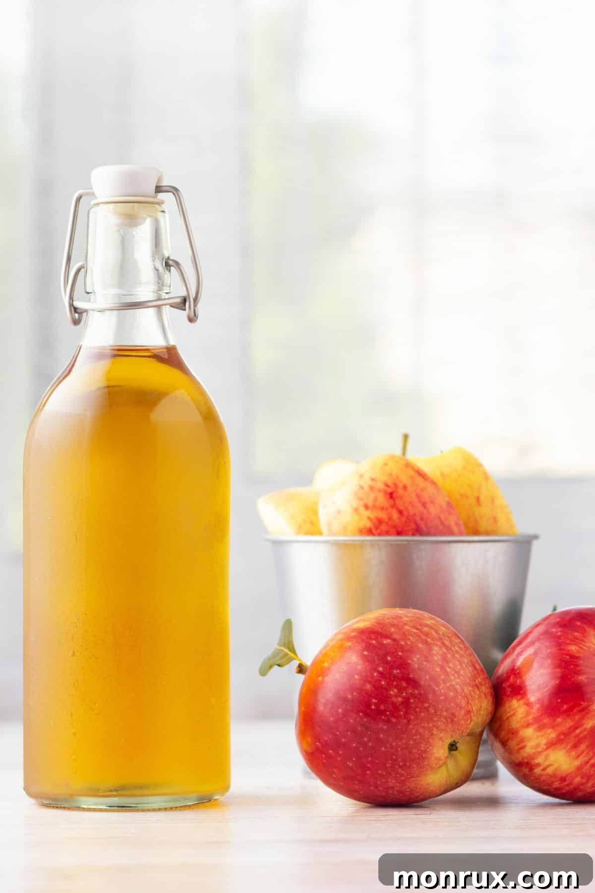A bottle of raw, unfiltered apple cider vinegar positioned next to a cluster of fresh red apples, symbolizing its natural origin.