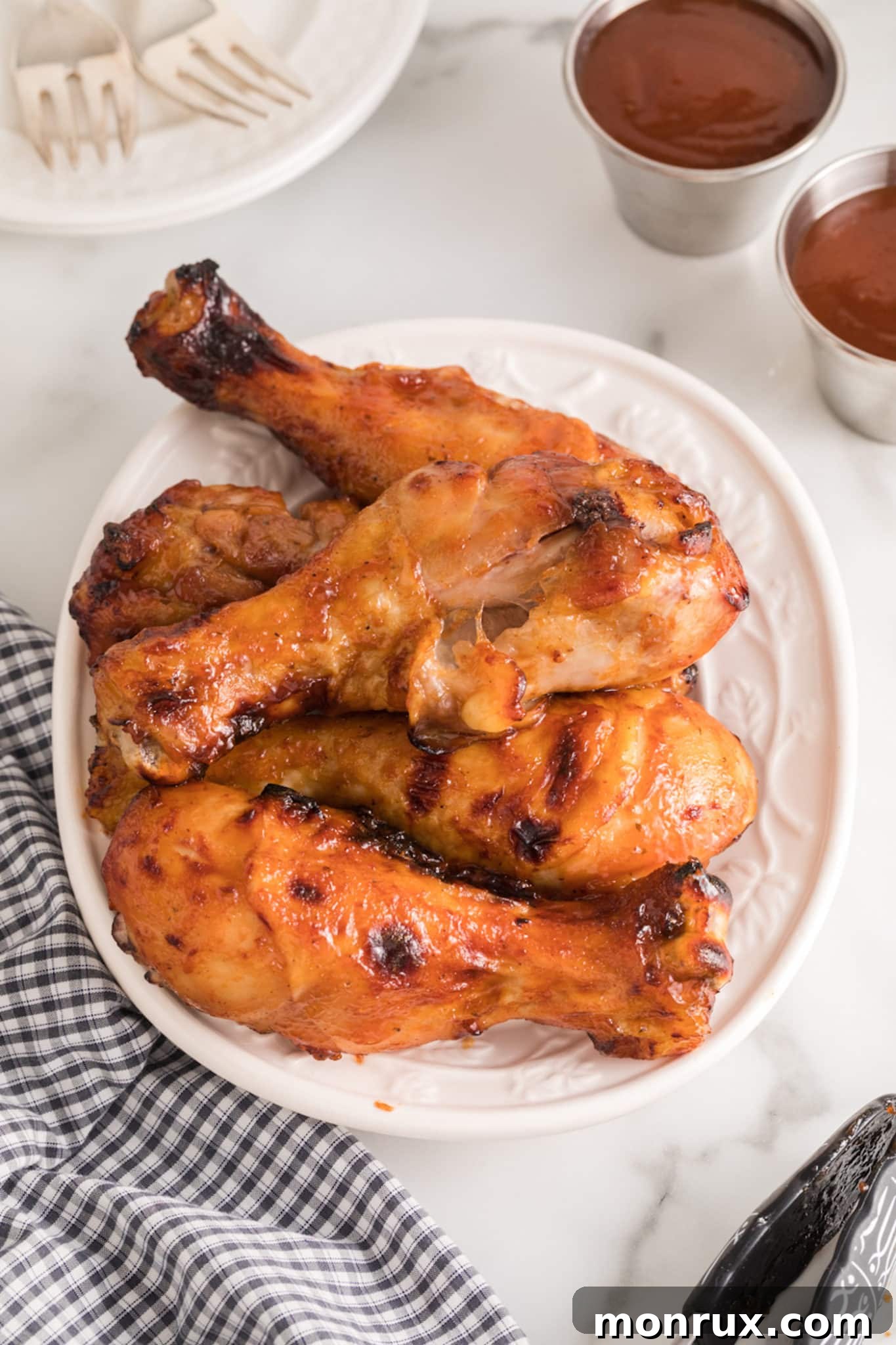 Air fryer BBQ chicken legs piled up on a white plate, ready to serve.