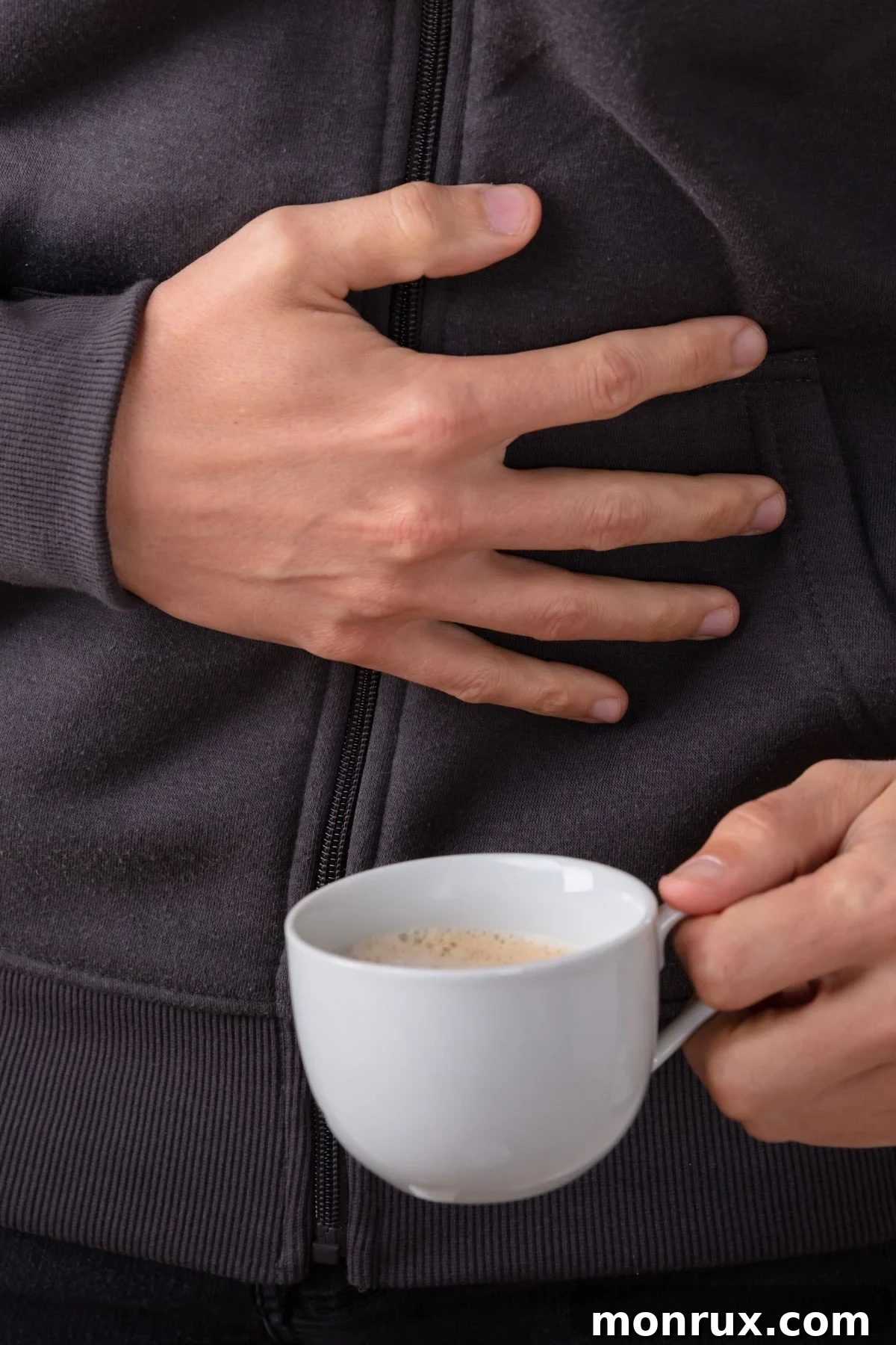 A person holding a cup of coffee with one hand and resting the other on their stomach, indicating digestive discomfort.