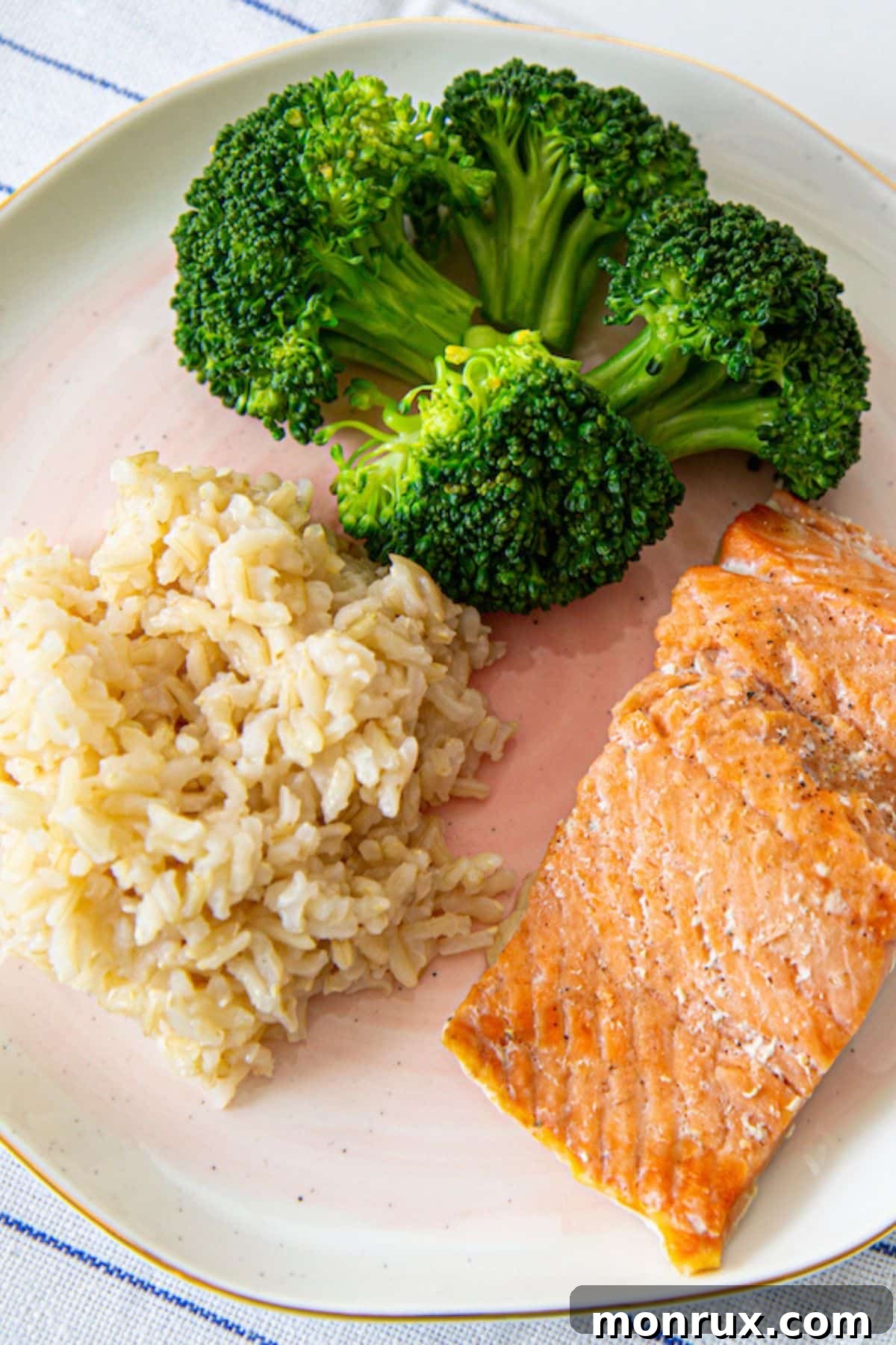 A serving of bone broth rice plated alongside steamed green broccoli and flaky baked salmon, highlighting a balanced and healthy meal combination.