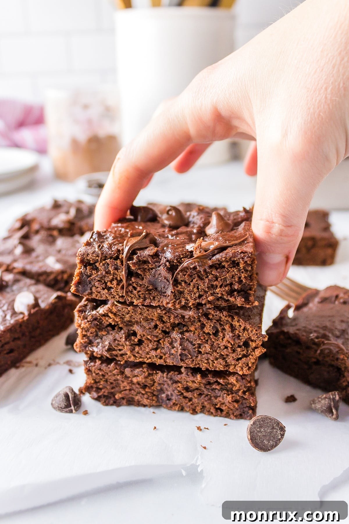 A hand reaching for a piece of freshly baked fudgy dairy-free brownie on a small white plate, emphasizing its enticing texture.