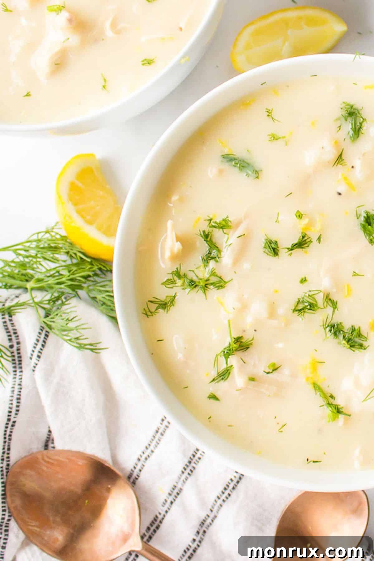 A beautifully presented bowl of creamy Avgolemono soup next to a serving spoon.