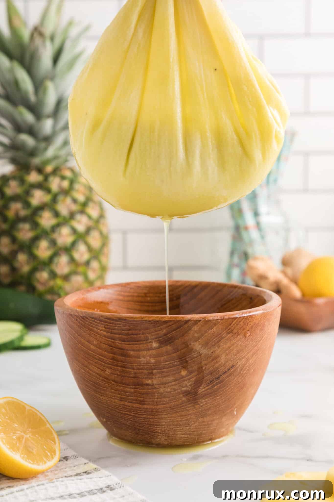 Straining pineapple ginger juice through a nut milk bag into a bowl.