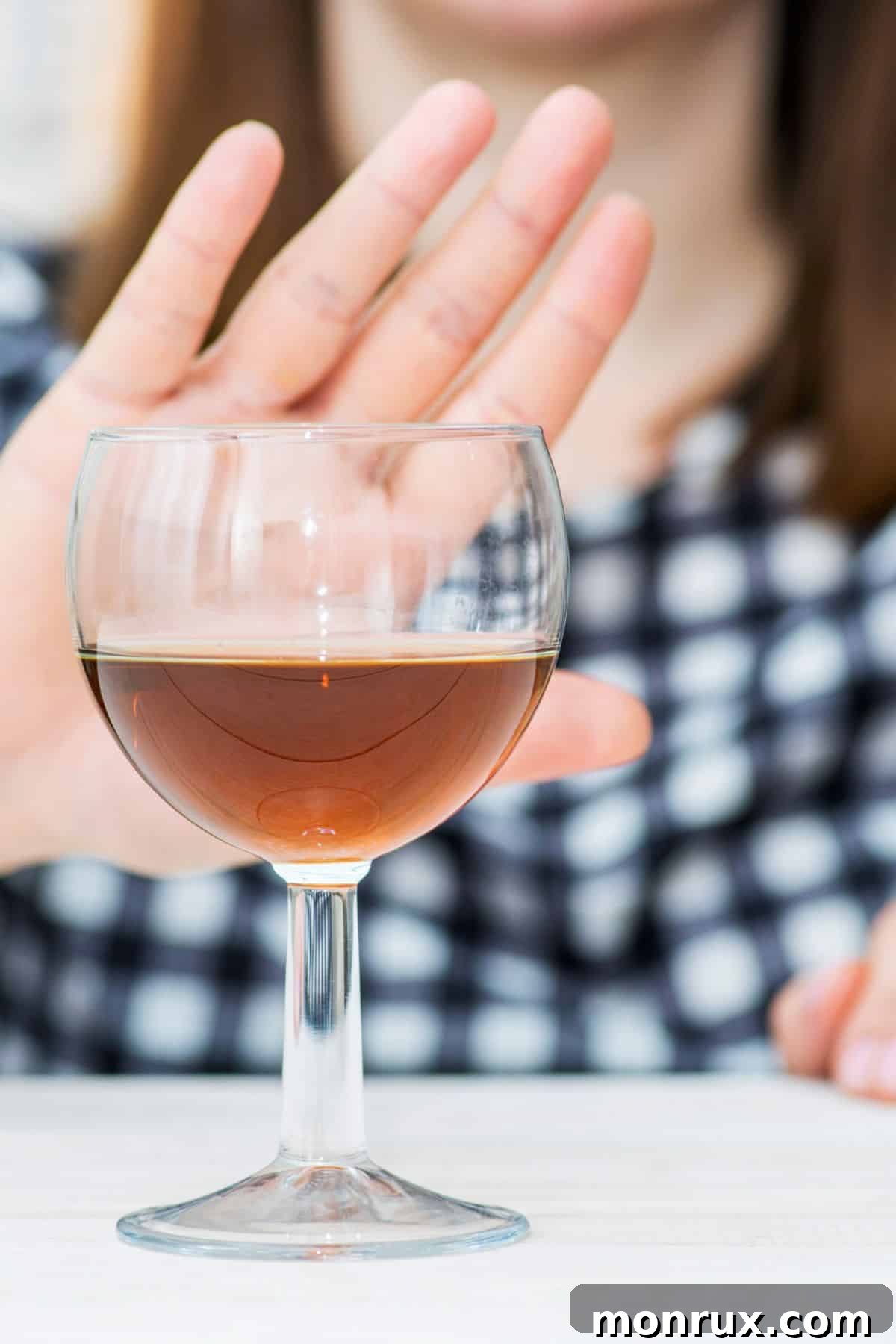 A woman holding her hand out in front of an alcoholic beverage, symbolizing a choice to avoid it.
