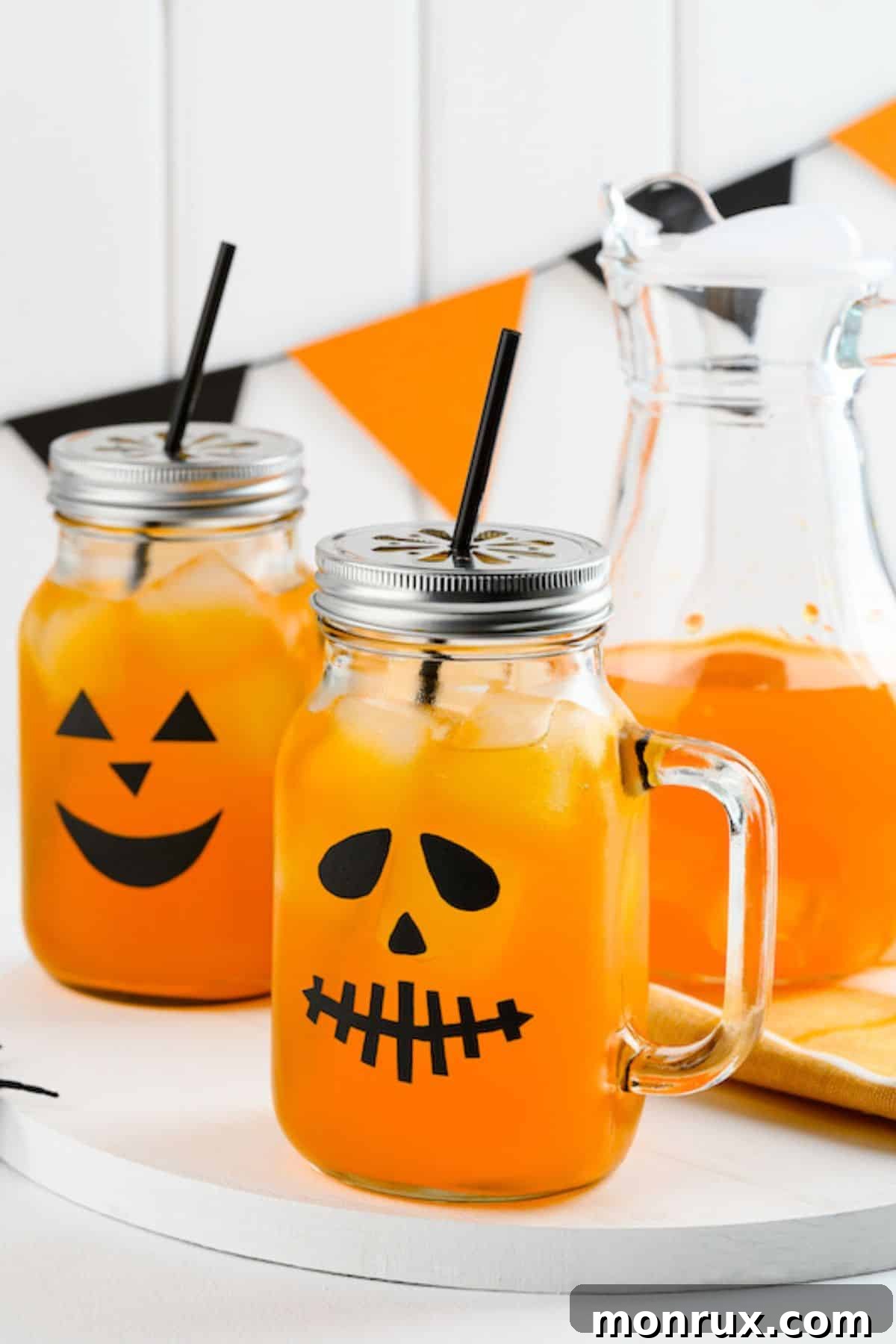 two pumpkin spice mocktails in jack-o-lantern jars, garnished with cinnamon sticks and apple slices.