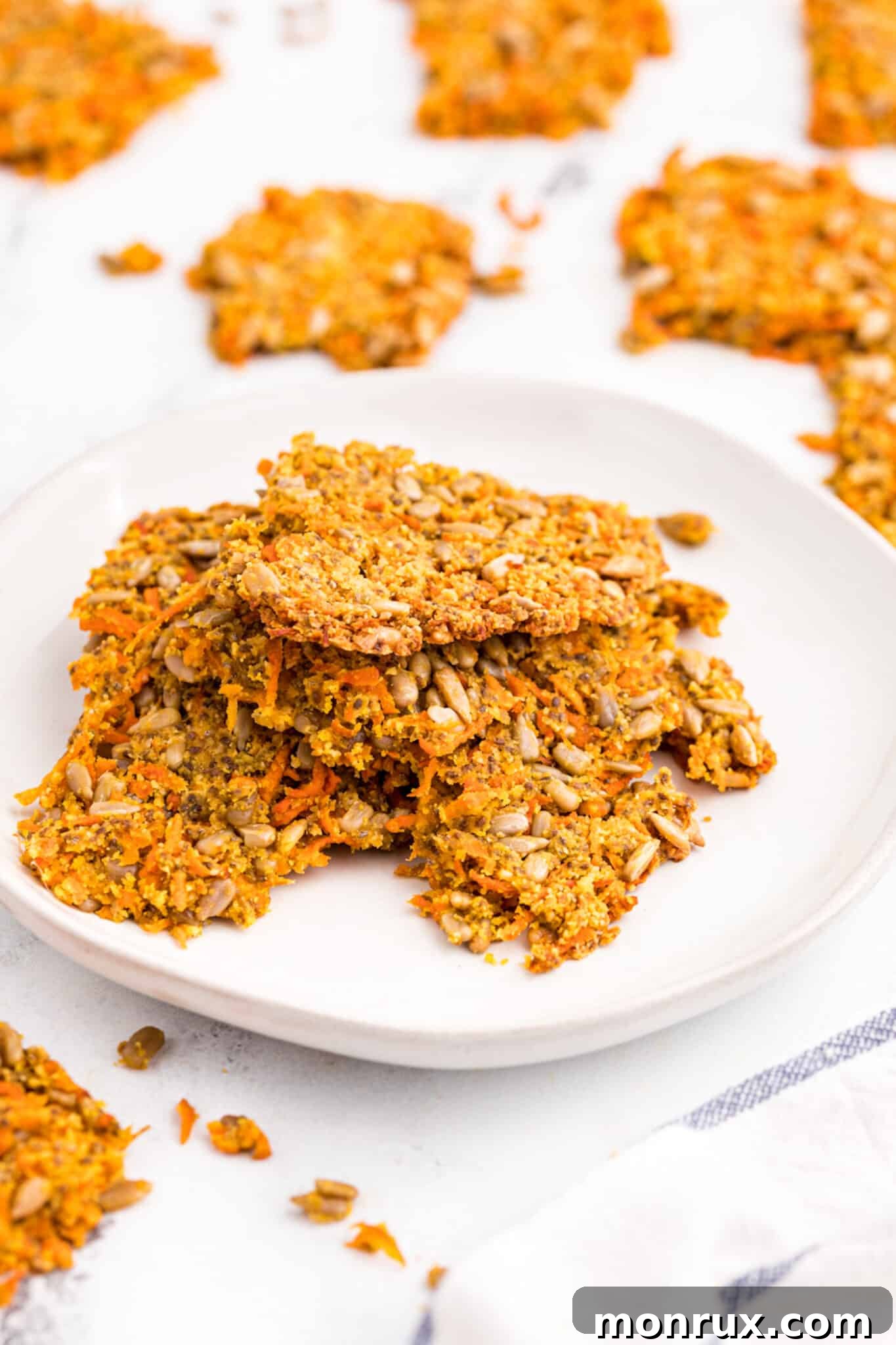 Crispy carrot crackers stacked artfully on a white plate, set on a rustic wooden tabletop.