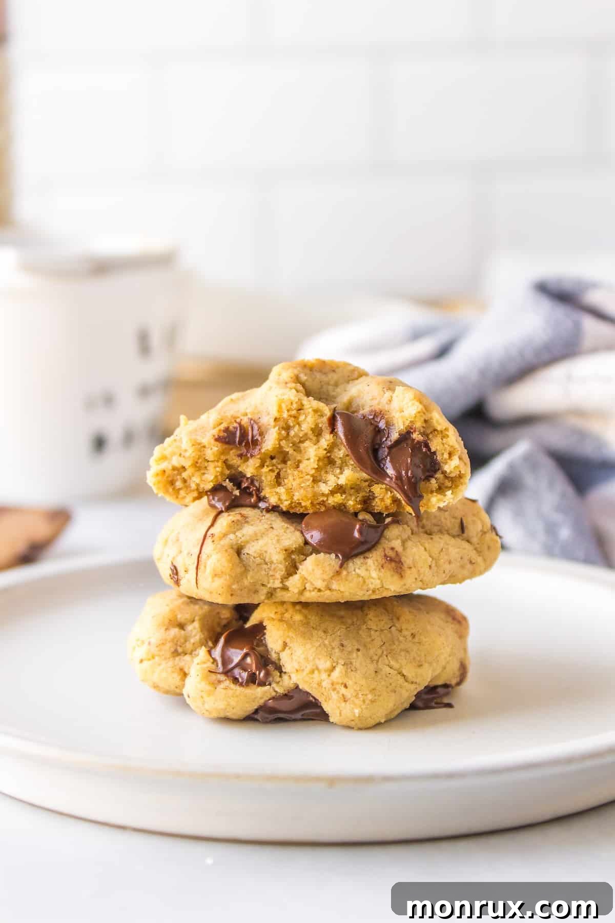 Three perfectly baked chocolate chip cookies without butter, stacked together on a white background, with a bite taken out of the top one.