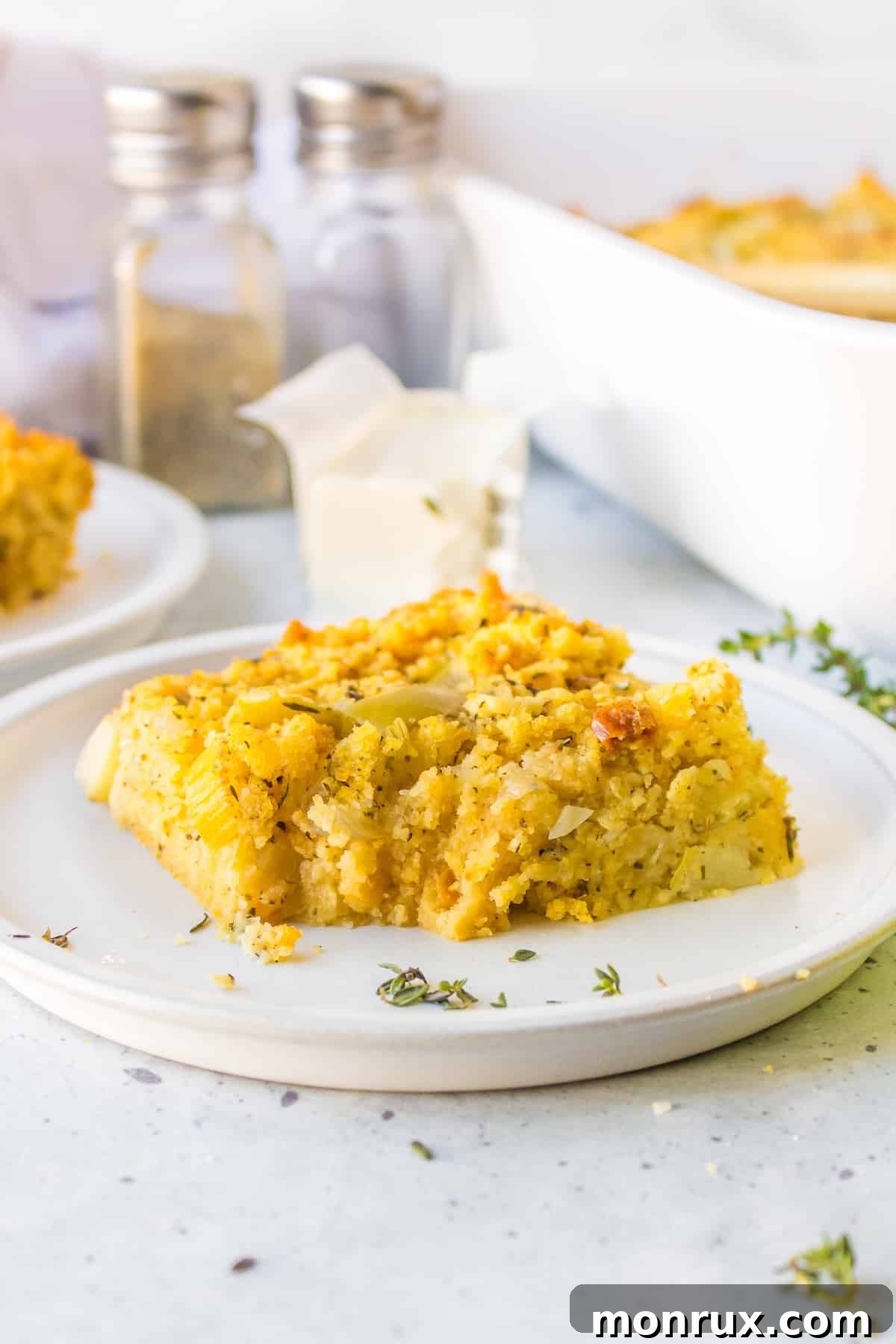 A perfectly baked slice of gluten-free cornbread stuffing on a clean white plate, garnished with fresh herbs.