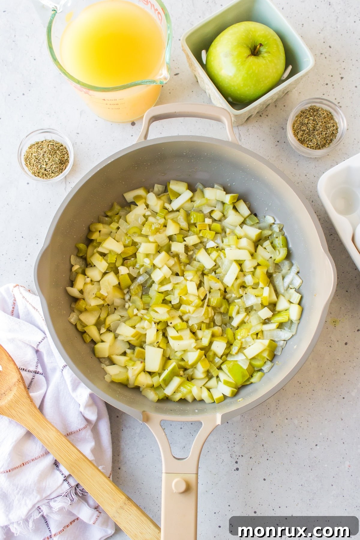 Sautéing chopped apple, onion, and celery in a large skillet for gluten-free cornbread stuffing.