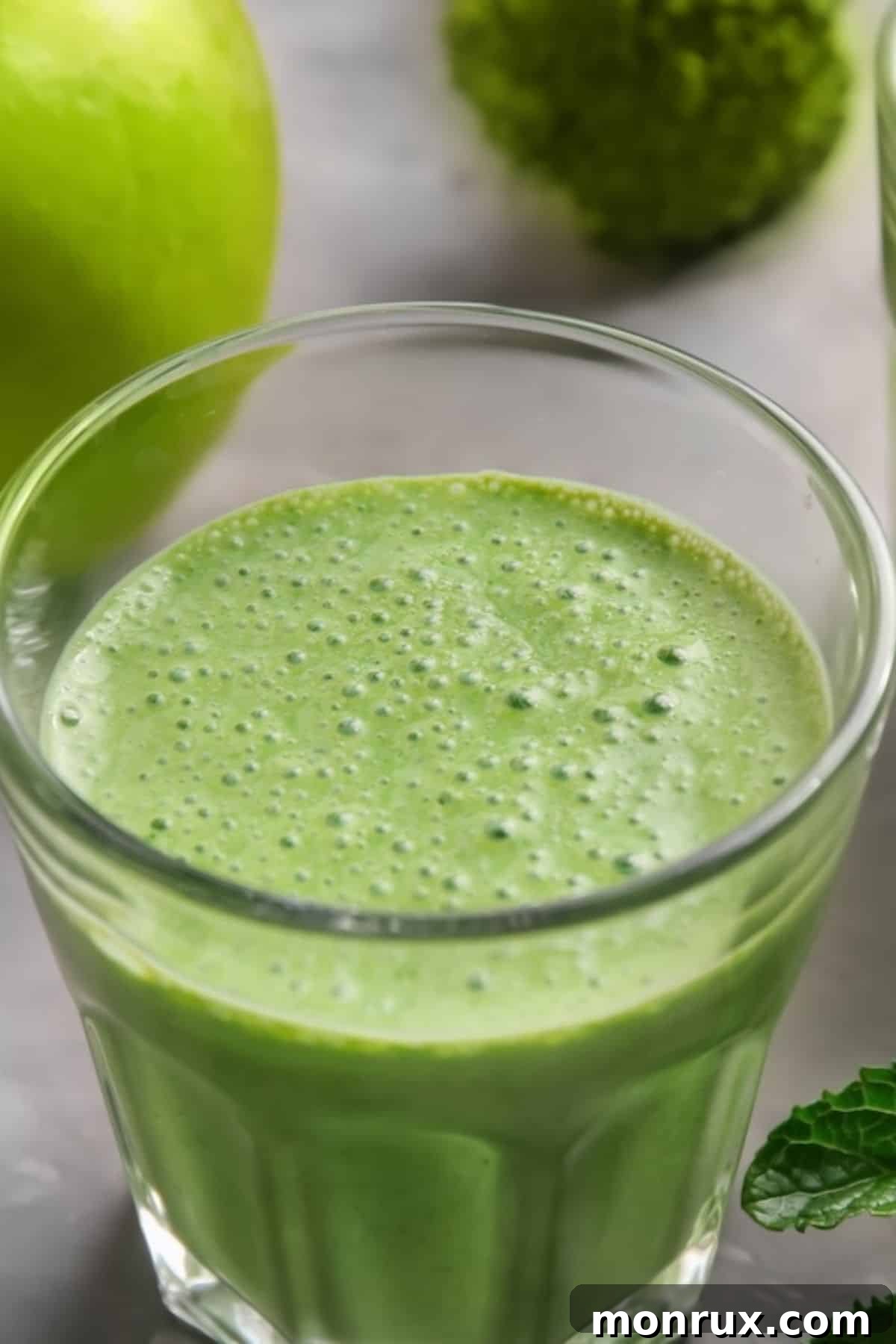 A large glass of vibrant green anti-bloat juice with a frothy top, showcasing its freshness.