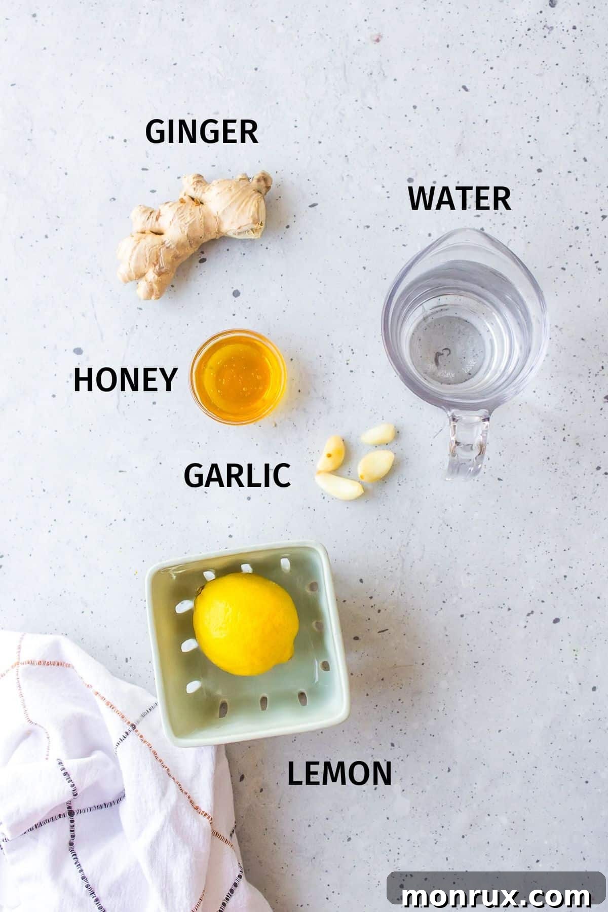 Arrangement of fresh ginger root, garlic cloves, a lemon, and a jar of honey on a kitchen counter, ready for making tea.