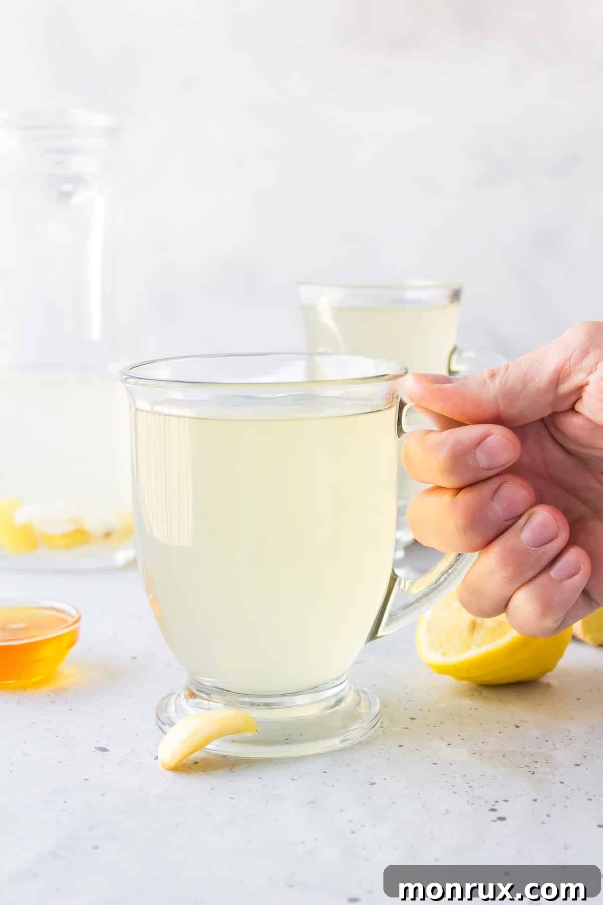 A person holding a clear glass mug of freshly made garlic tea, highlighting its warm color and steam.