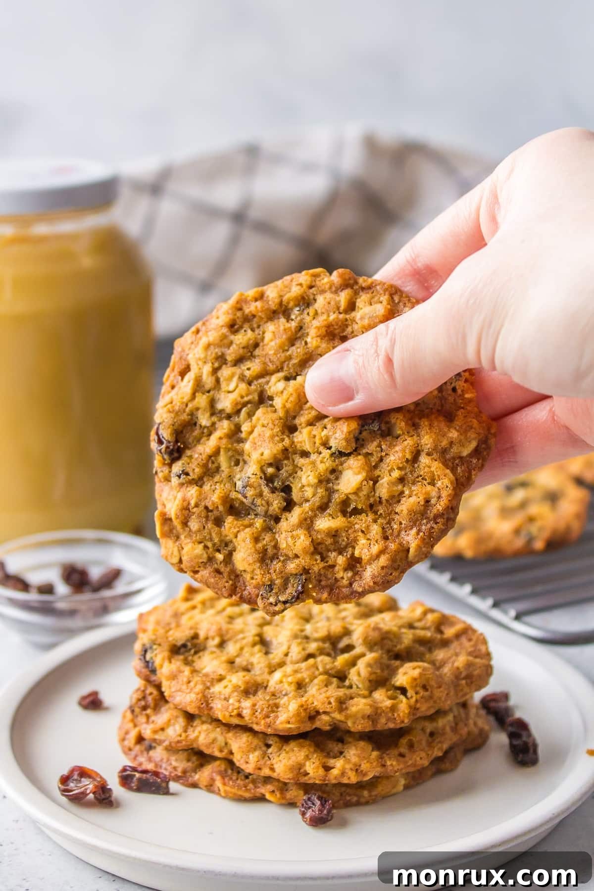 A person holding a freshly baked, warm oatmeal cookie, showing its texture and golden color.