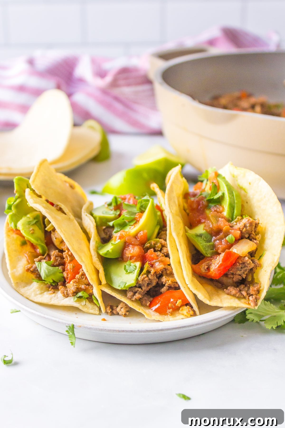 three bison tacos on a white plate, garnished with fresh cilantro and a lime wedge.