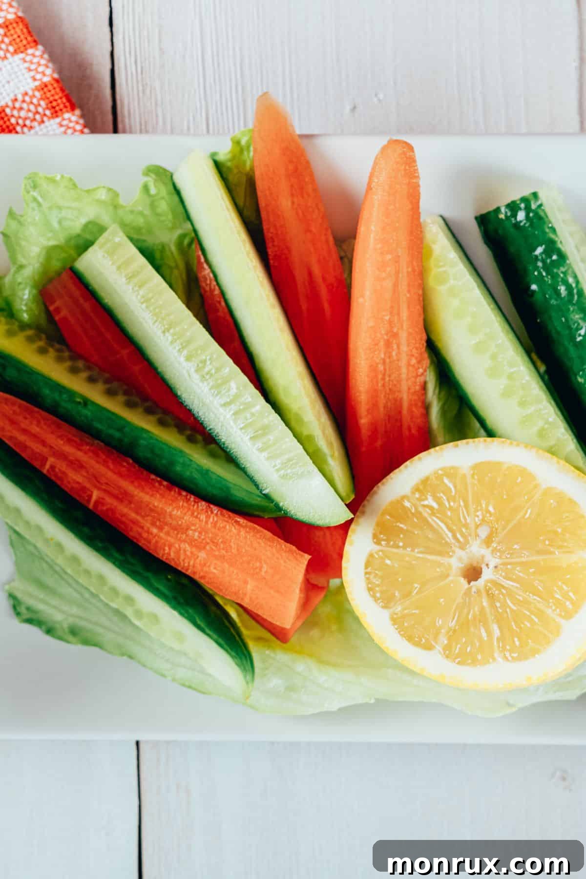 A vibrant plate featuring an assortment of colorful raw vegetables, including carrot sticks, cucumber slices, bell pepper strips, and cherry tomatoes, elegantly garnished with a lemon wedge.
