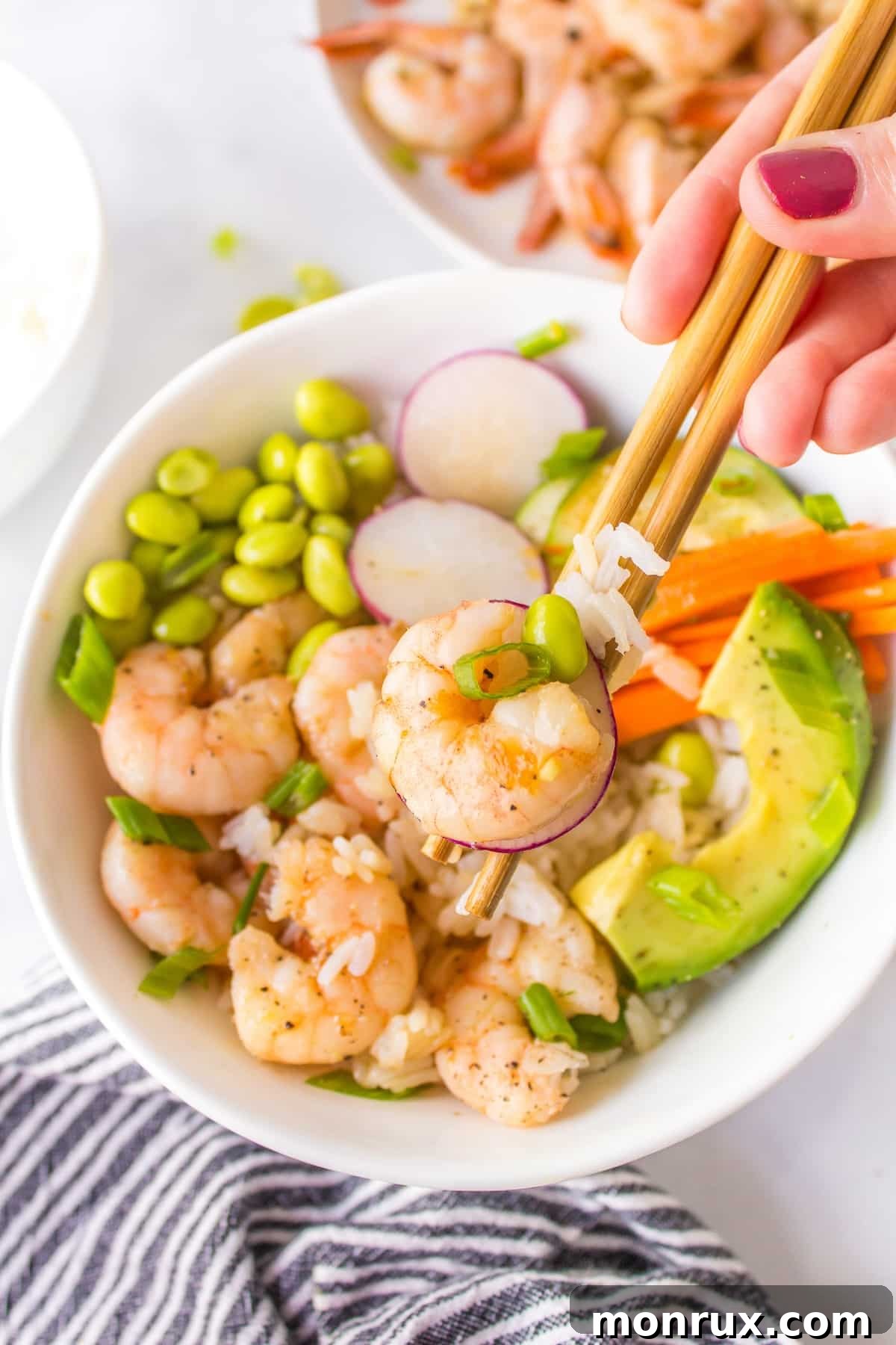 Chopsticks holding a delicious bite of a shrimp poke bowl, showcasing the vibrant ingredients.