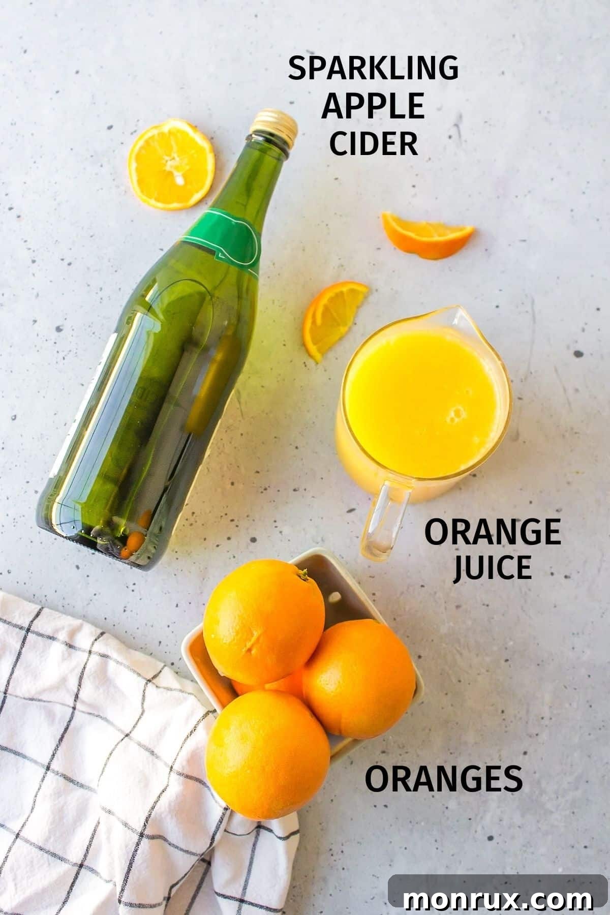 Fresh oranges and a bottle of sparkling apple cider, the two main ingredients for a mimosa mocktail, laid out on a kitchen surface.