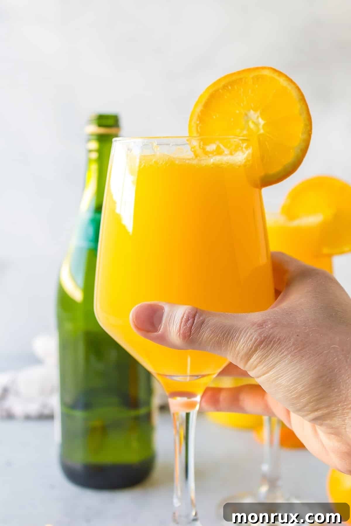 A hand gracefully holding a glass of Mimosa Mocktail, highlighting its inviting color and refreshing appeal.