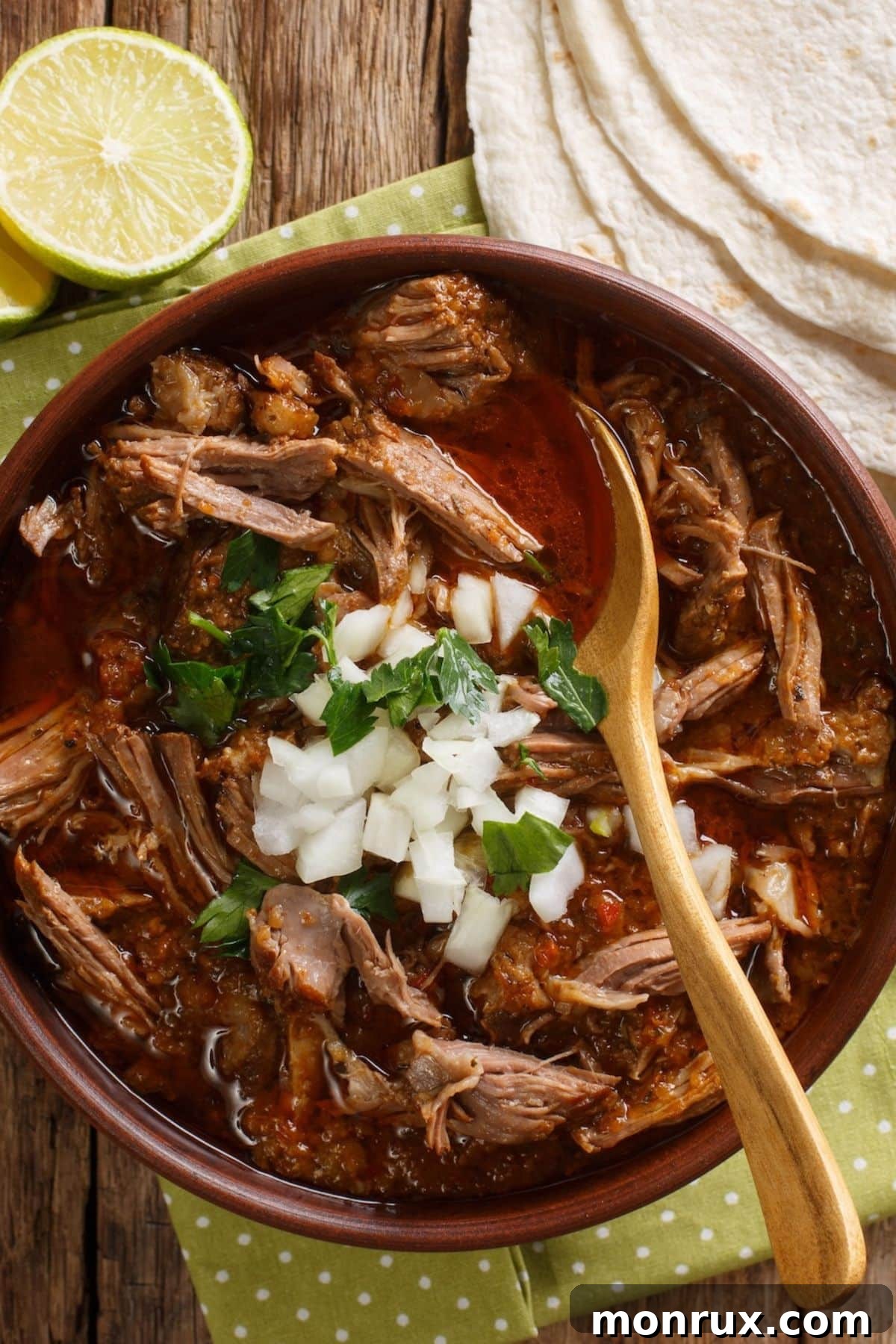 A vibrant bowl of Mexican birria stew, generously topped with fresh cilantro and finely chopped white onions, served alongside warm corn tortillas for dipping.