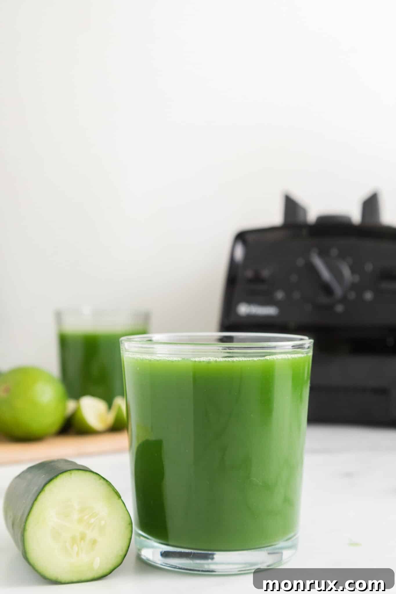 glass of cucumber juice on countertop with blender in background.