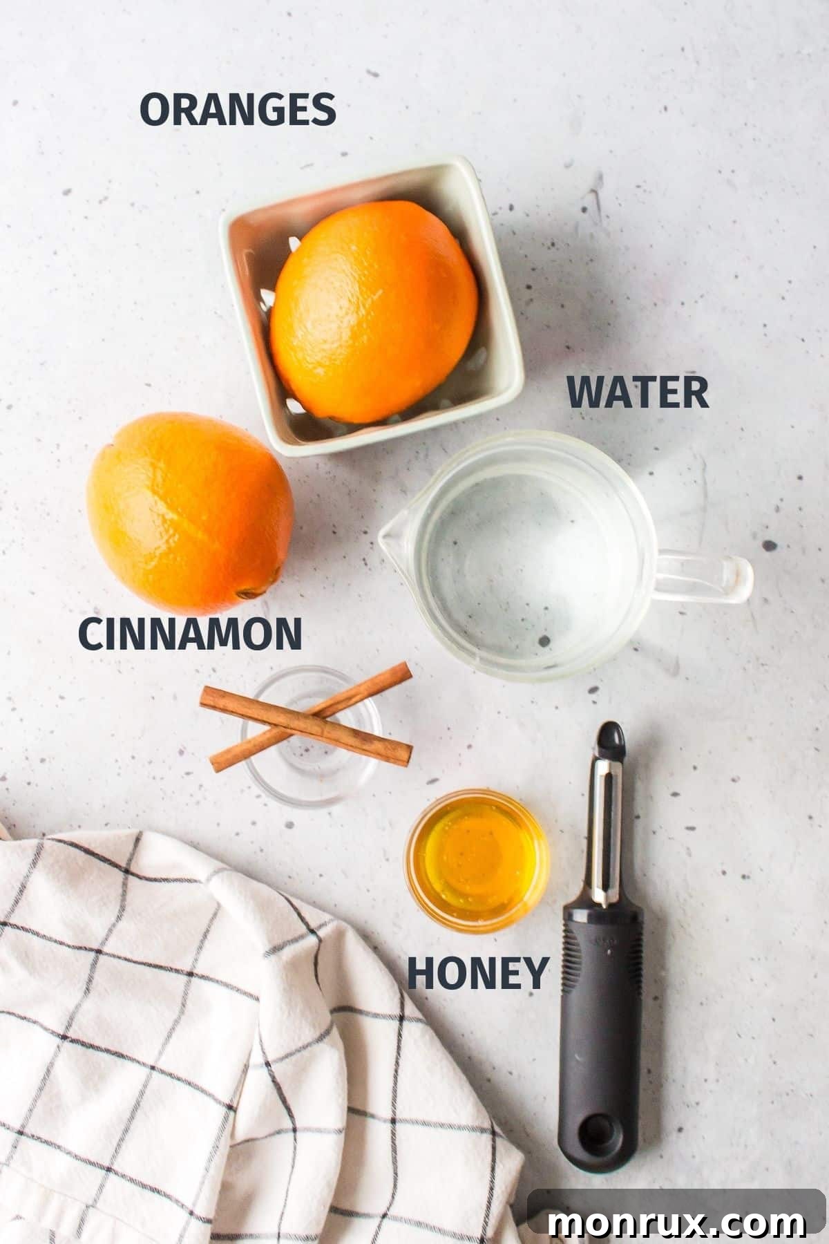 A collection of ingredients for orange peel tea, including fresh oranges, a cinnamon stick, and a jar of honey, arranged on a rustic wooden countertop.